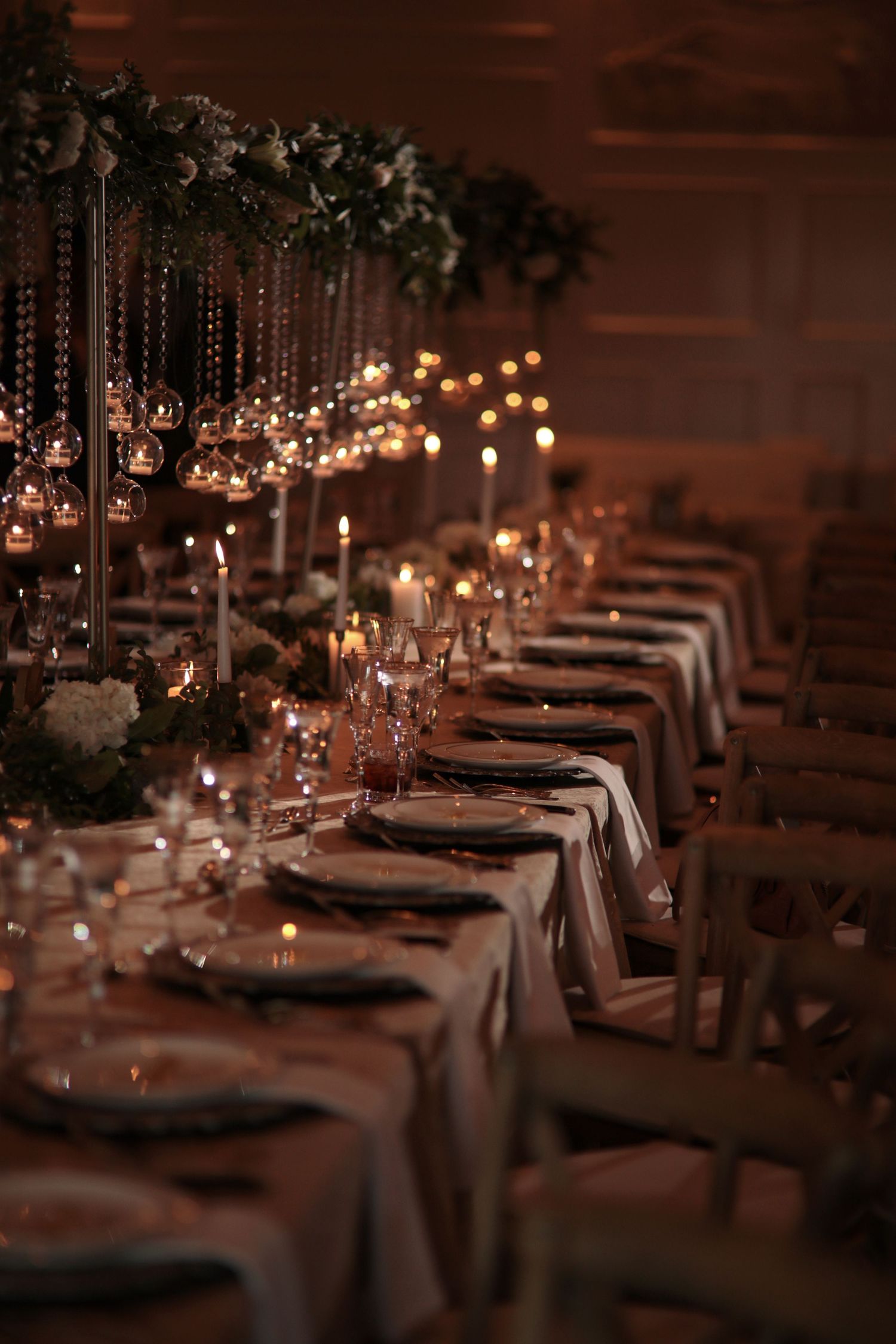 Flores & pine Calgary wedding reception setting with crystal glasses, white linens and hanging floral decorations illuminated by candlelight