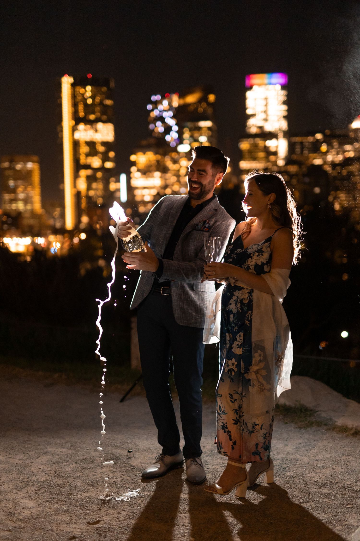 Engaged couple enjoying champagne while looking at illuminated city skyline at night in Calgary Canada