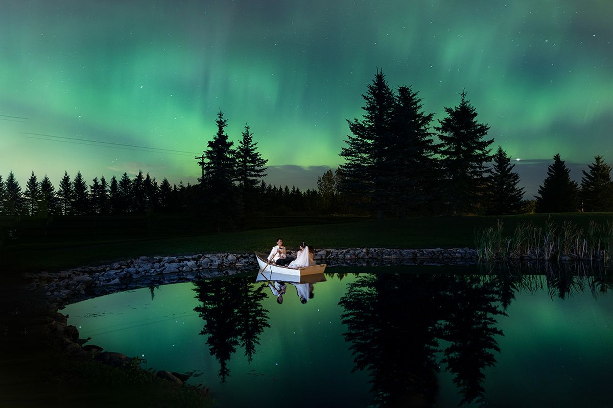 A bride and groom sit under Northern Lights in a rowboat on their wedding night at Pine and Pond Wedding venue in Ponoka Alberta