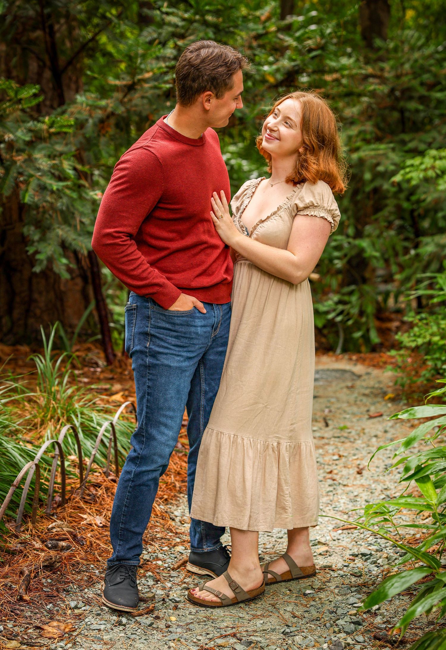 Couple walking and laughing together on a gravel path surrounded by lush greenery.