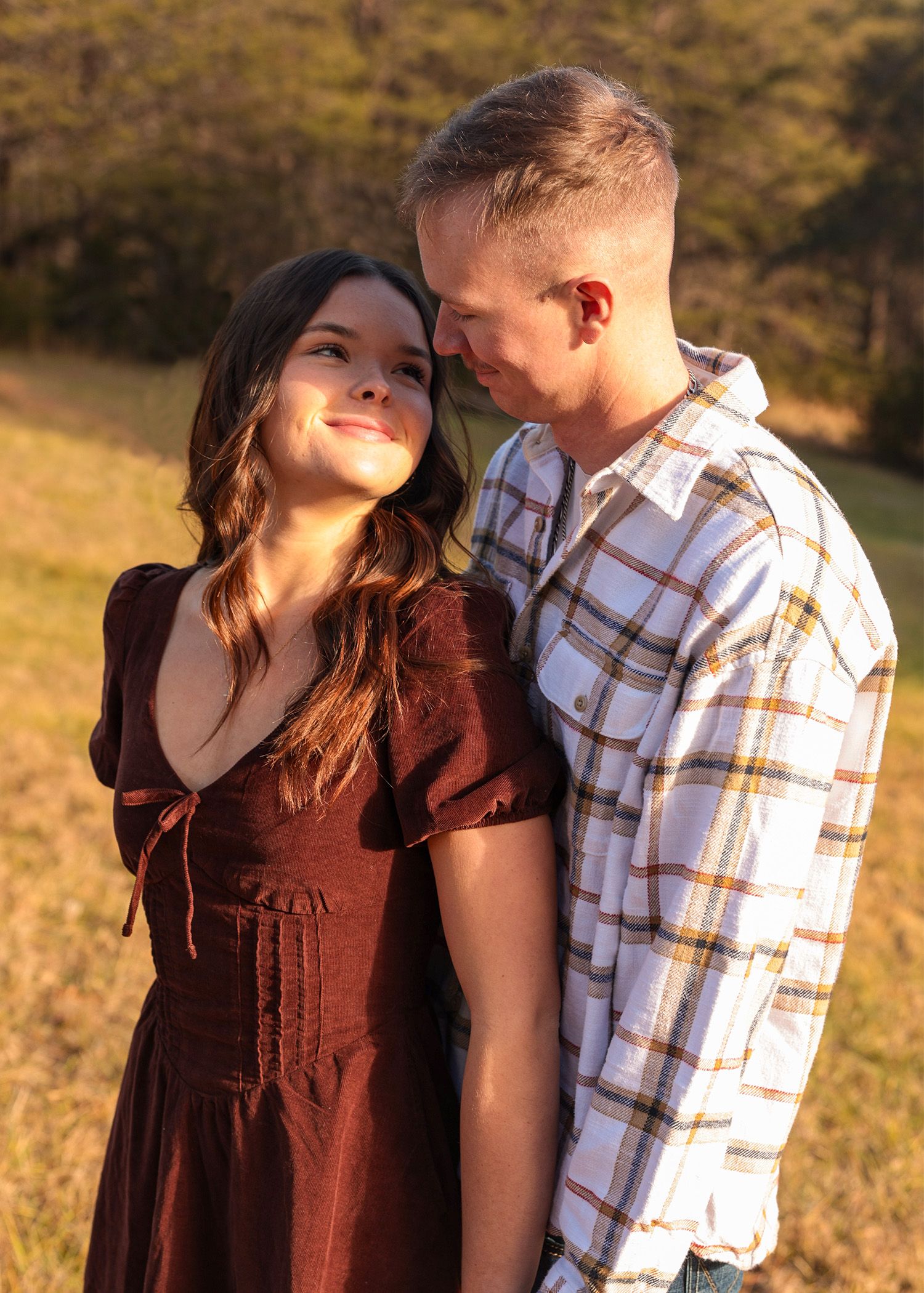 Romantic outdoor photoshoot in golden field with couple in coordinated brown and plaid outfits.