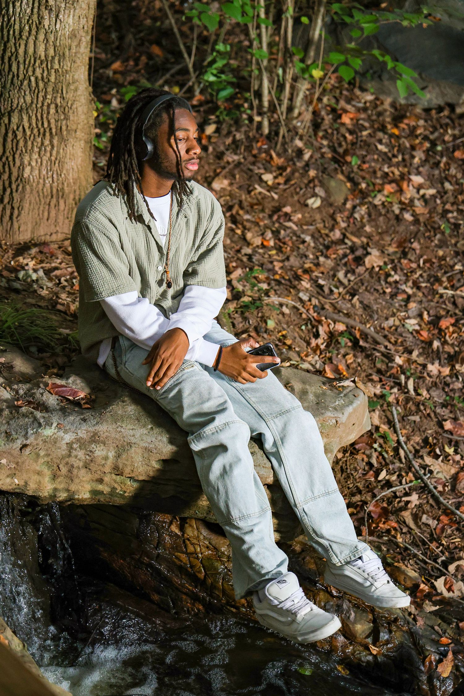 Person lounging on fallen tree trunk wearing light denim and gray vest in forest setting.