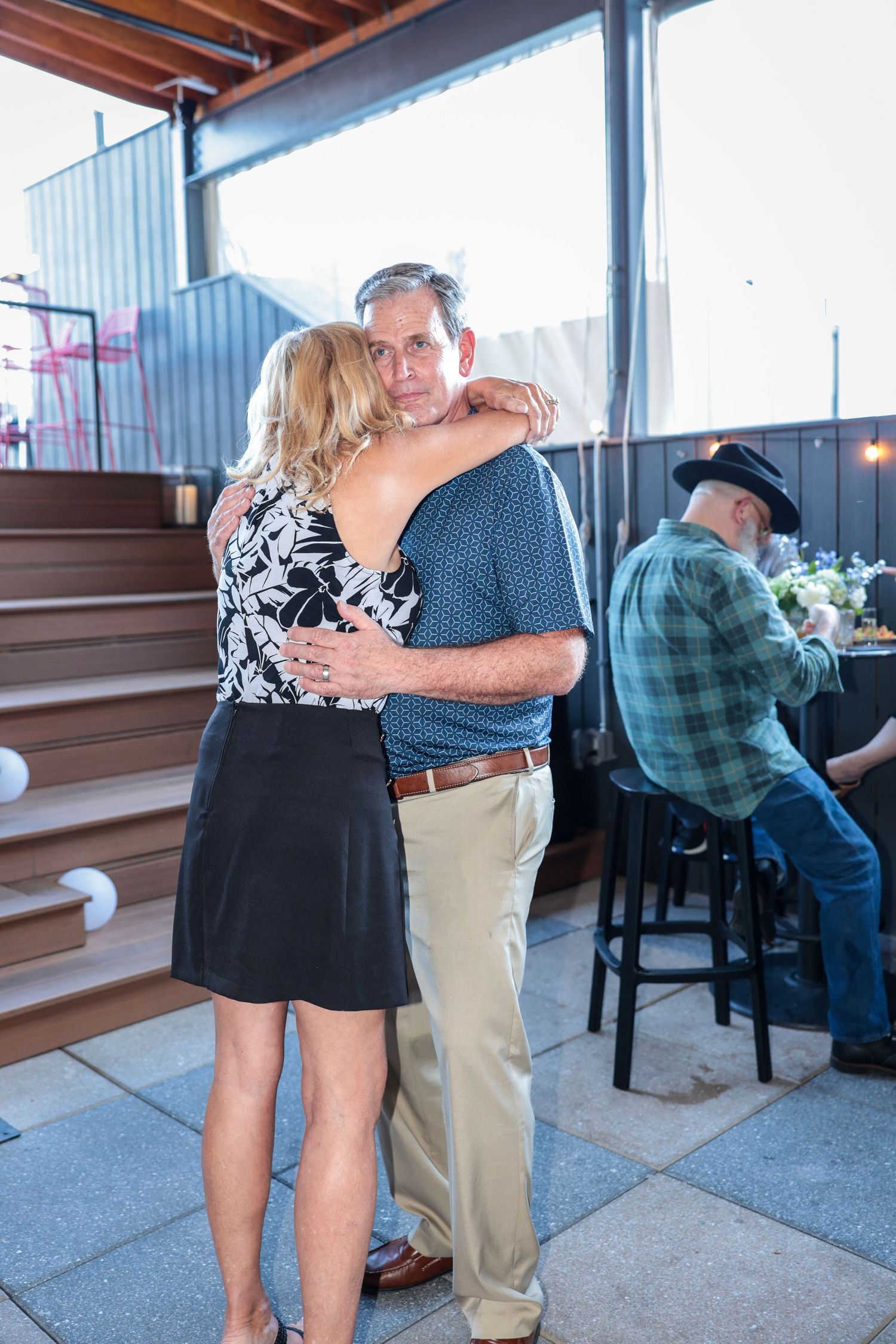 A couple embraces while dancing at an indoor venue with a bar in the background.