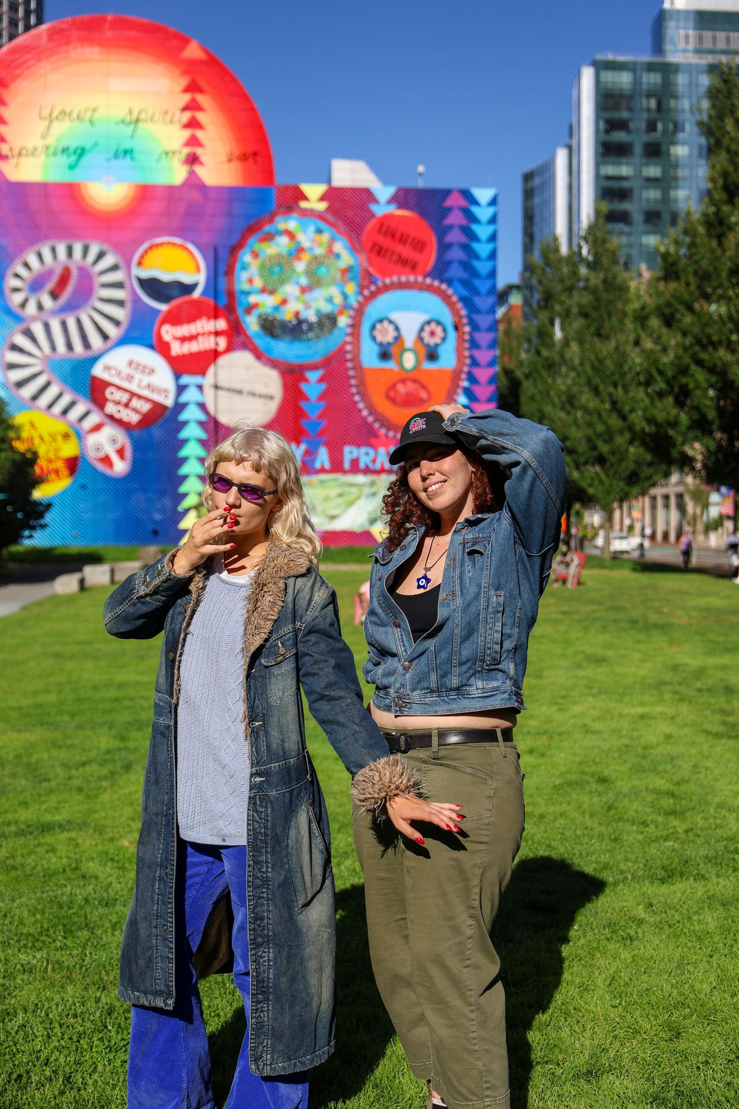 Two people dancing and having fun on grass with colorful mural backdrop in city park.