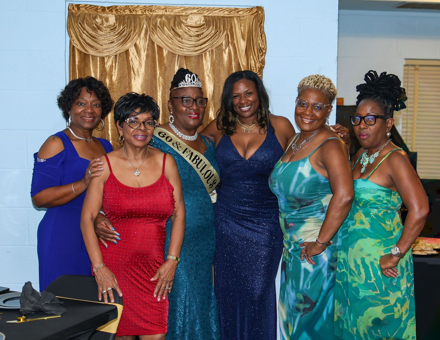 A group of six people in formal attire pose together at an event with gold curtains in the background.