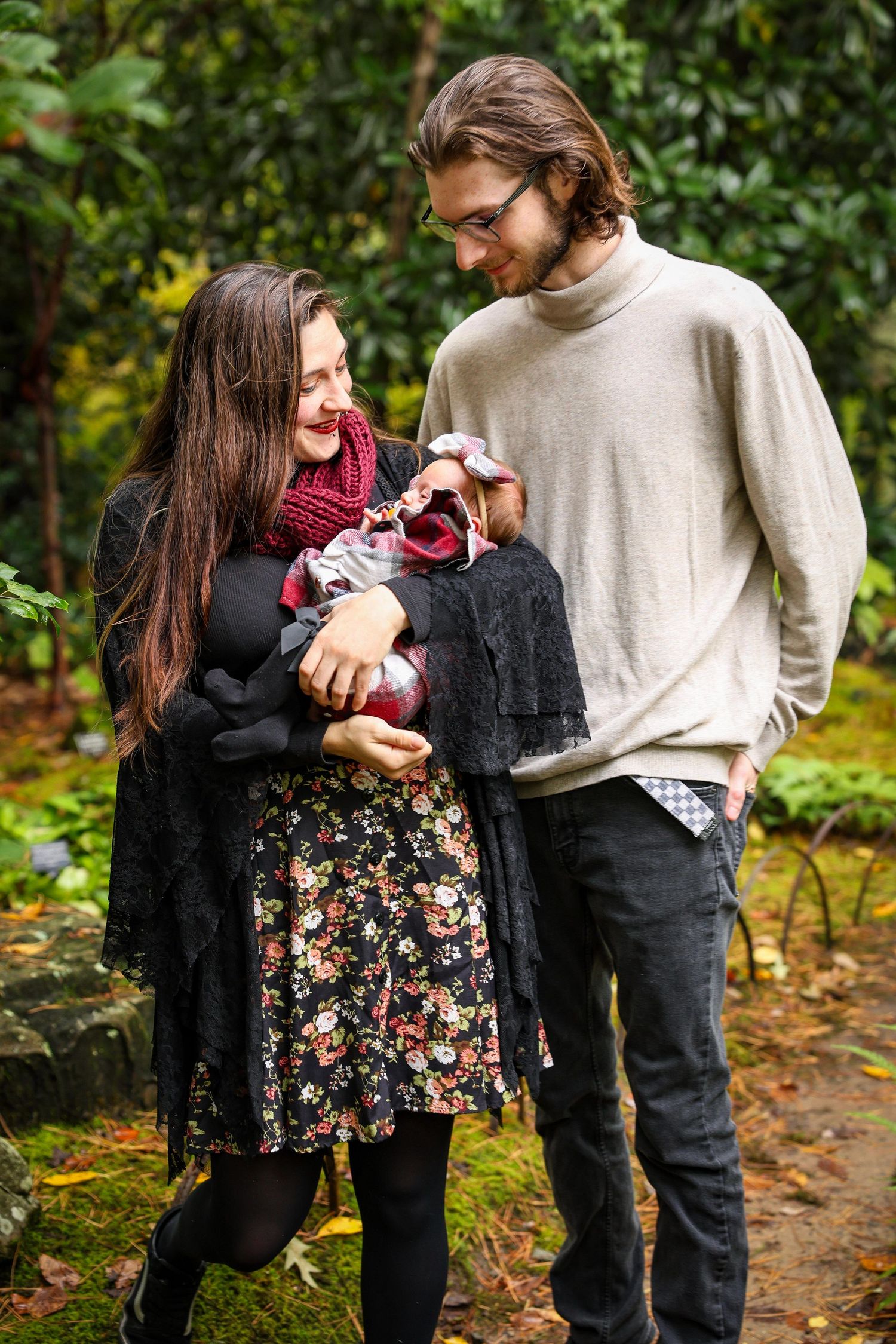 Couple in warm sweaters admiring baby outdoors in autumn setting.