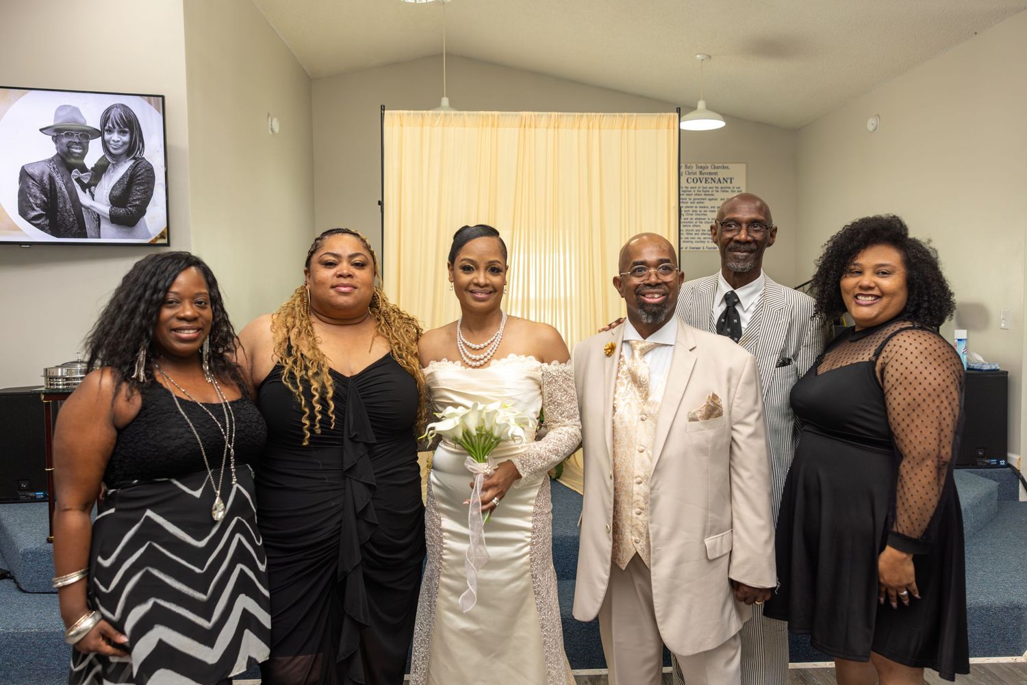 Wedding party posing together in a church, bride in white gown holding bouquet with family in formal attire.