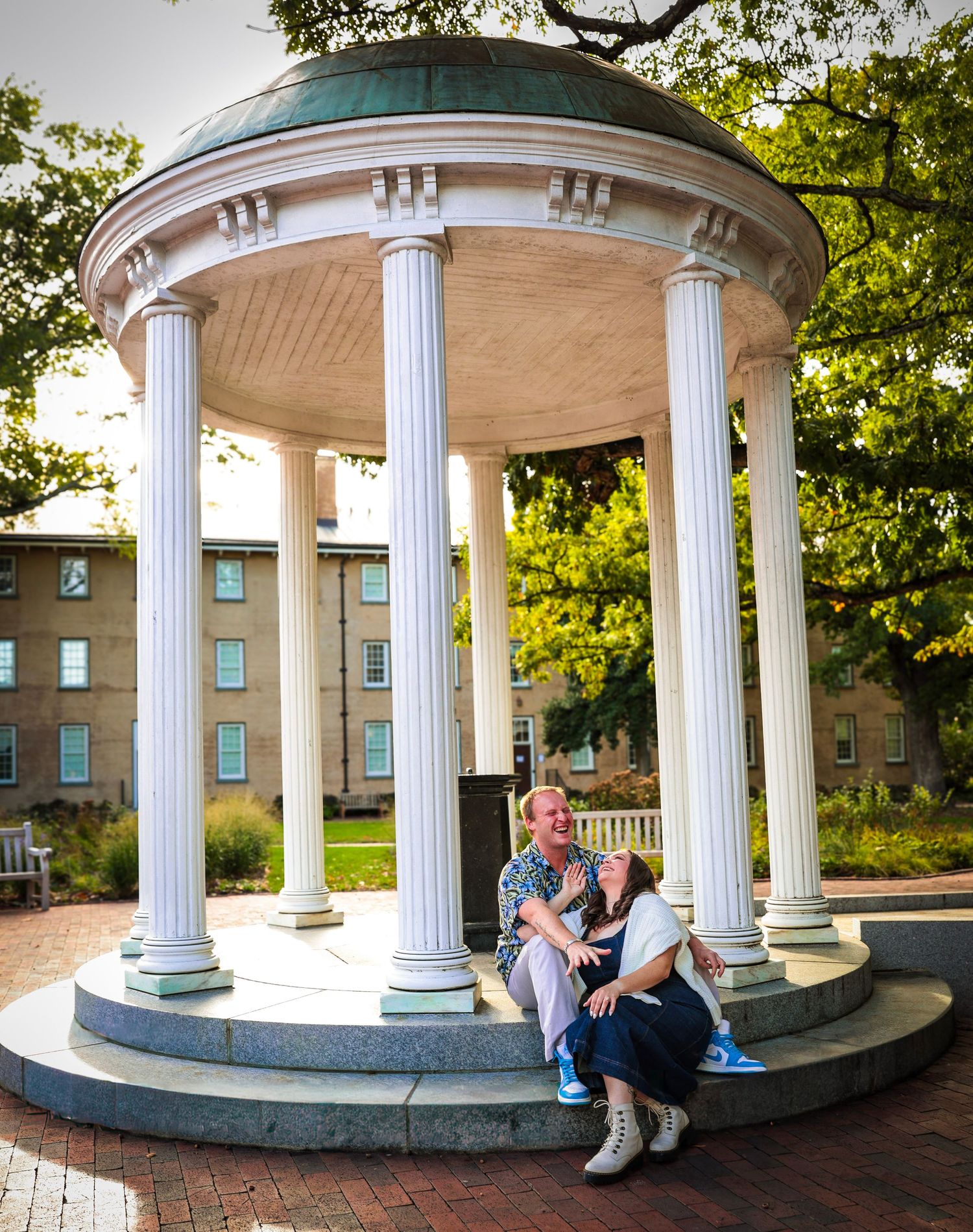 A romantic photoshoot under a classical white gazebo with columns on a brick pathway.