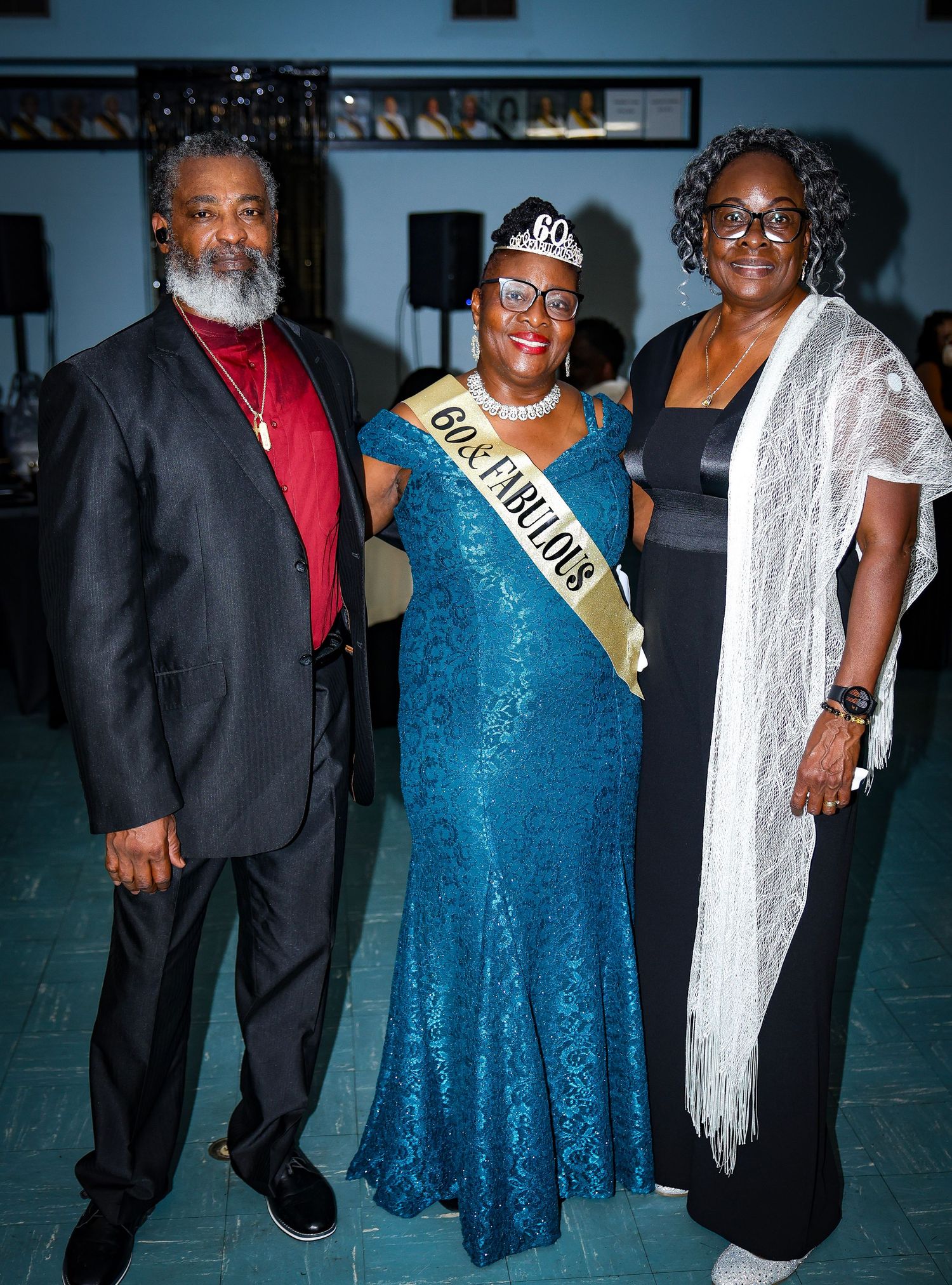 Formal event guests in elegant gowns and suits pose together under party decorations.
