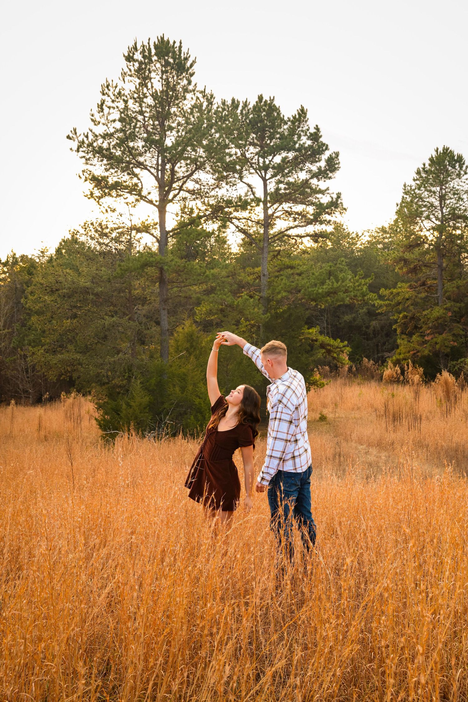 Romantic couple enjoying sunset in tall autumn grass with pine forest backdrop.