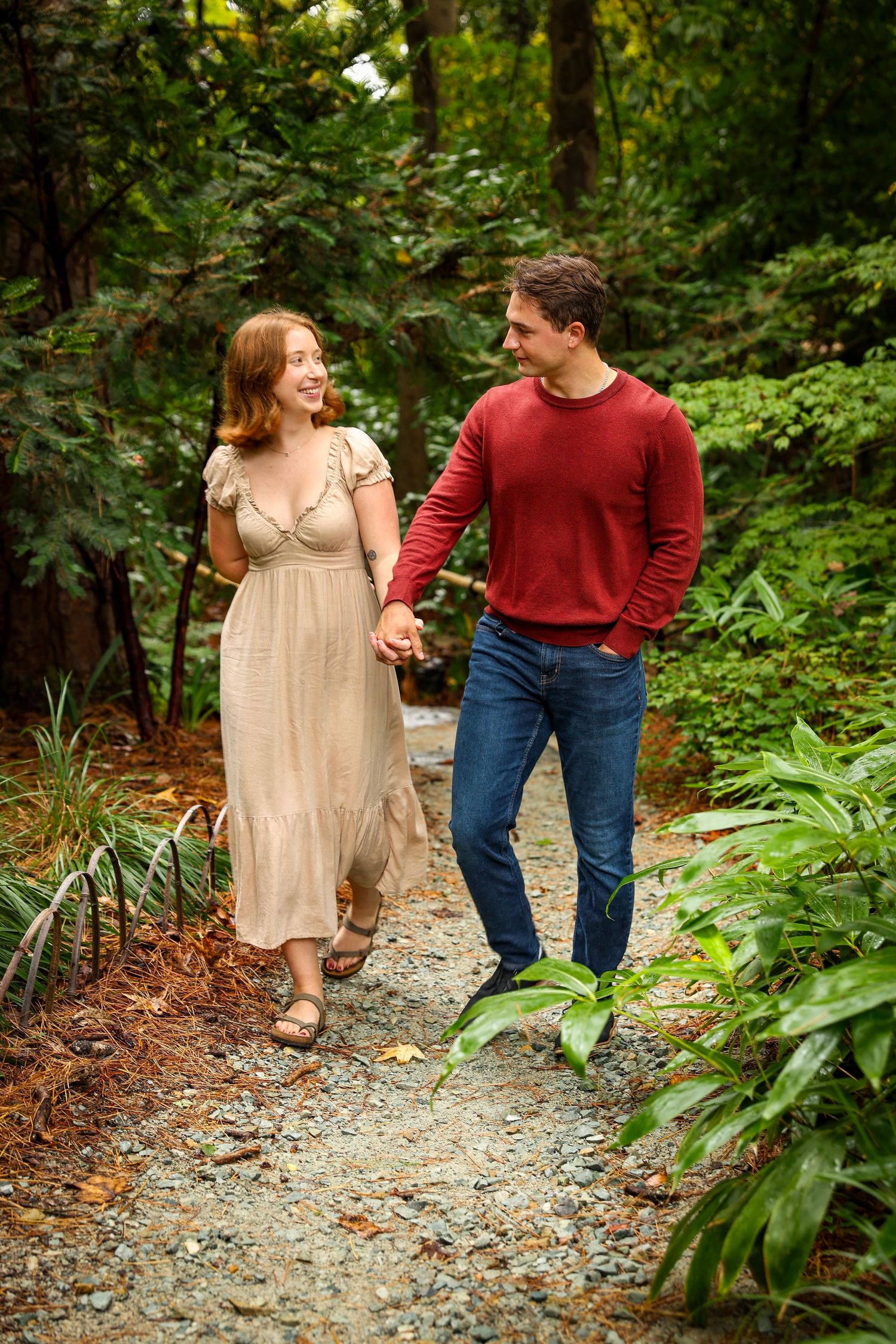 Couple walking and sharing laughs on a gravel path through a wooded garden setting.
