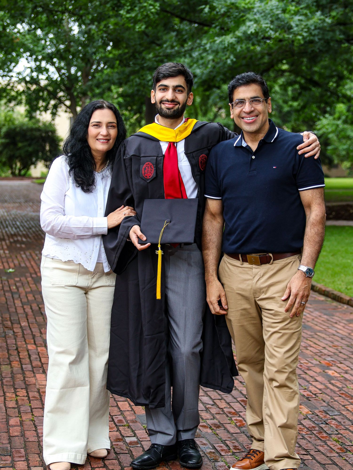 A graduate in cap and gown poses with family members on a brick walkway.