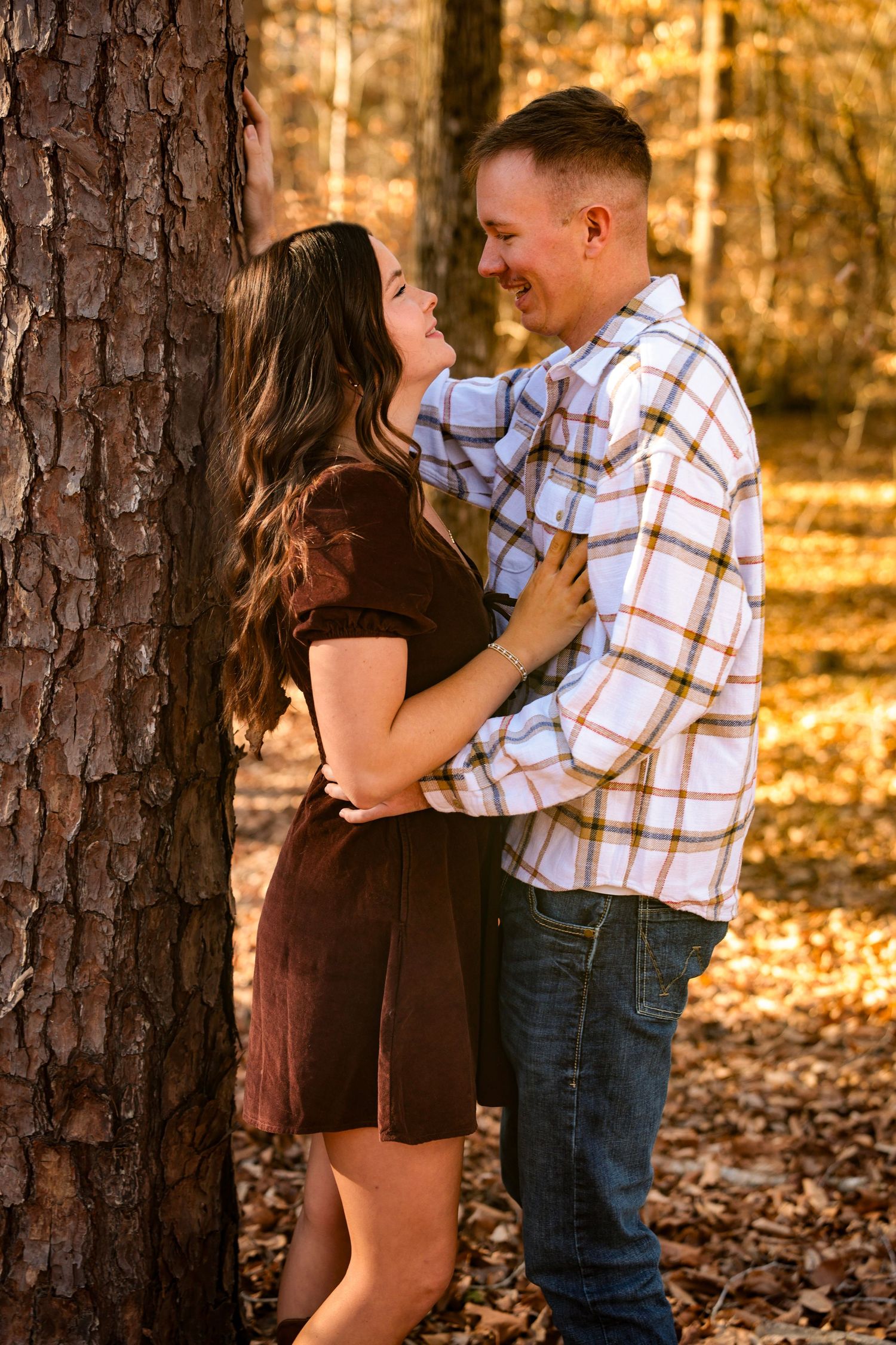 Intimate couple portraits against tree trunks in warm autumn lighting.