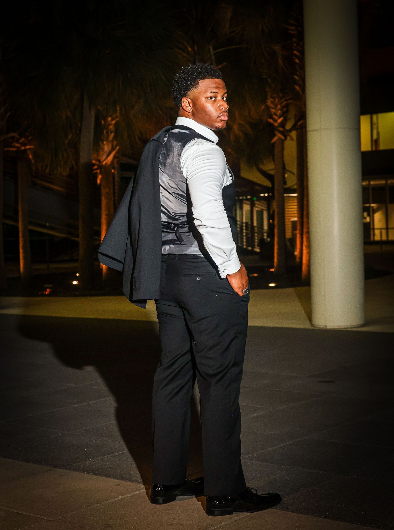 A figure in formal attire stands in a dimly lit space with dramatic shadows.