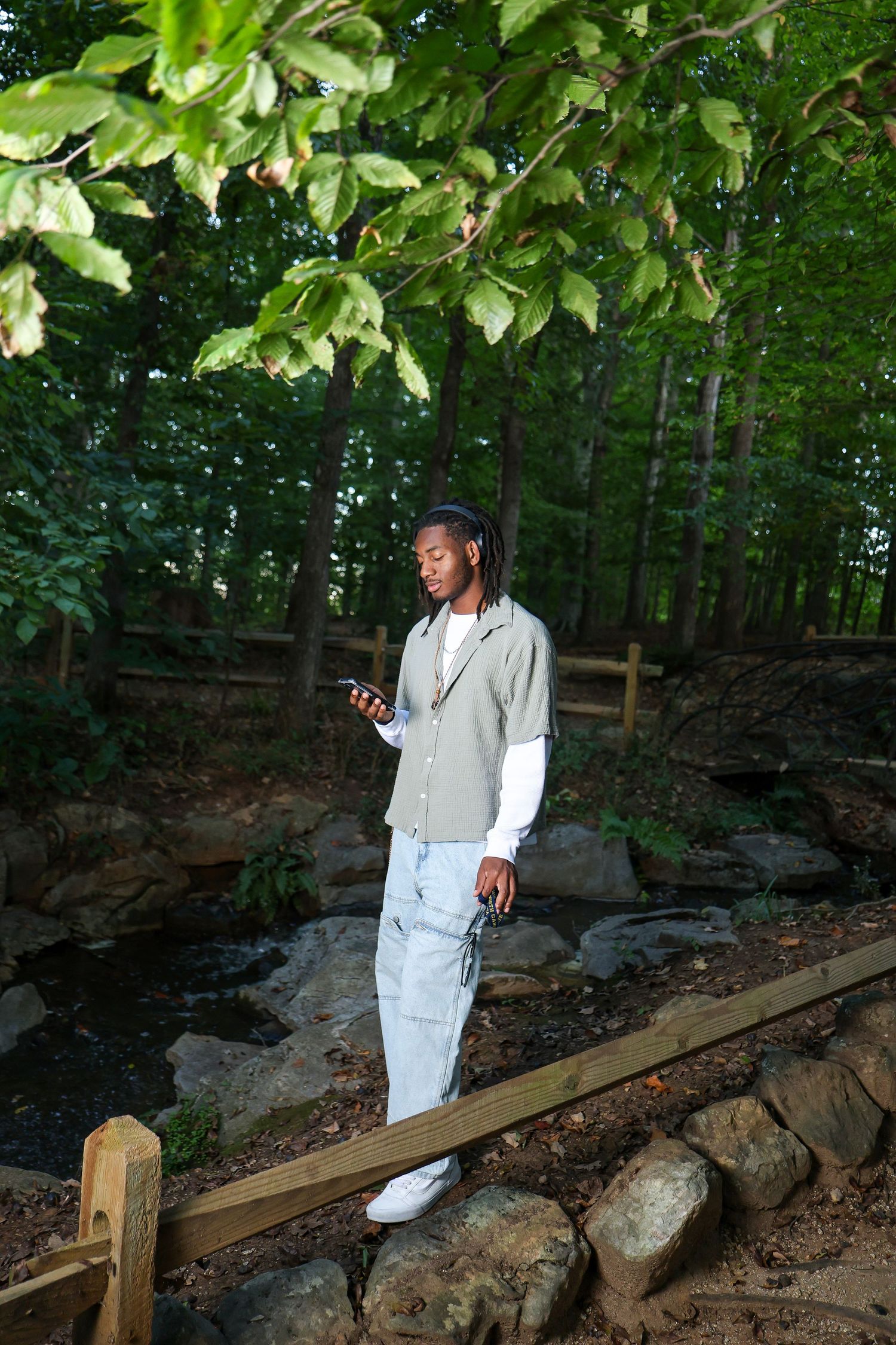 Person in light colored outfit standing near wooden railing in lush green forest setting.