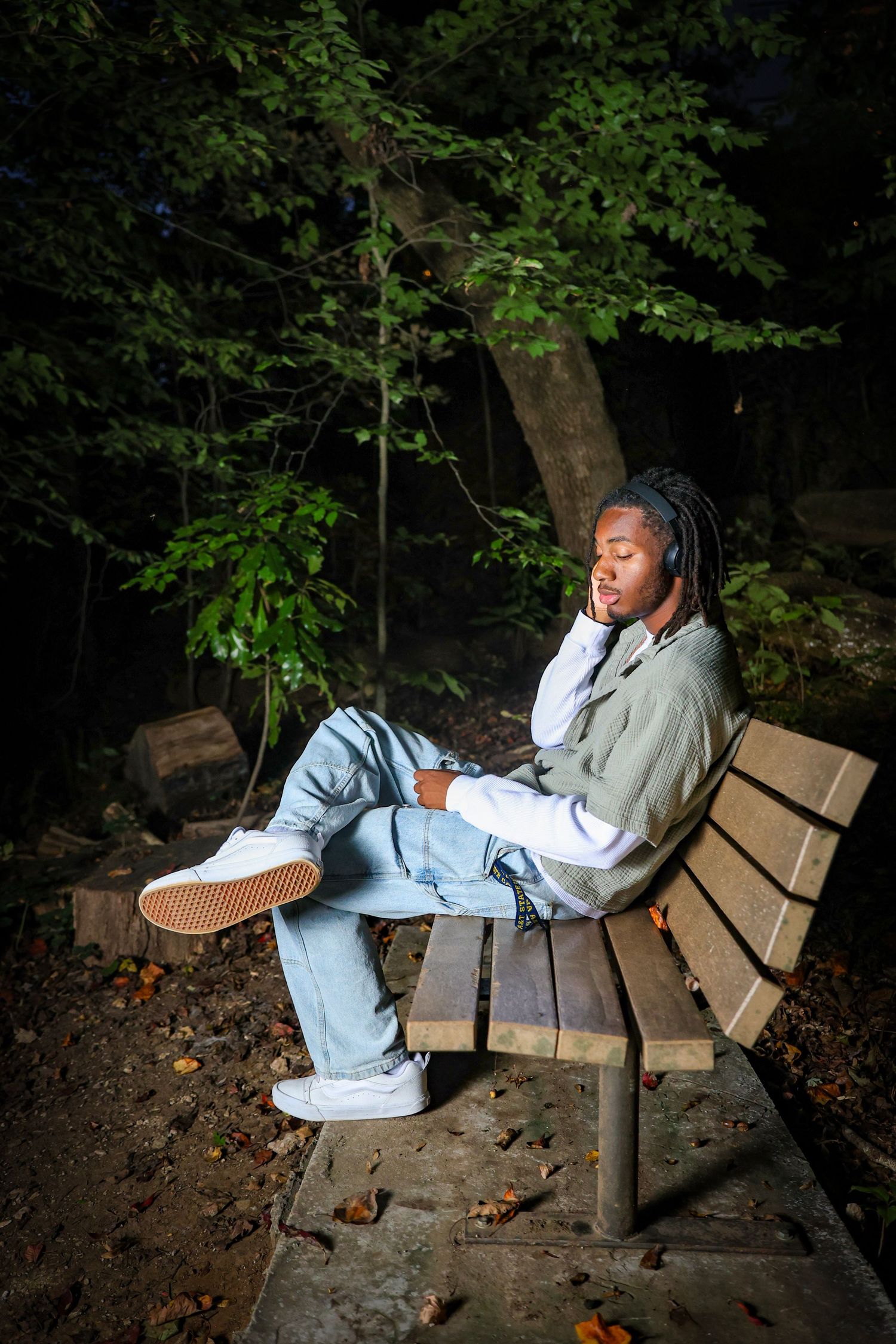 Person relaxing on park bench wearing casual attire and white sneakers in wooded area.
