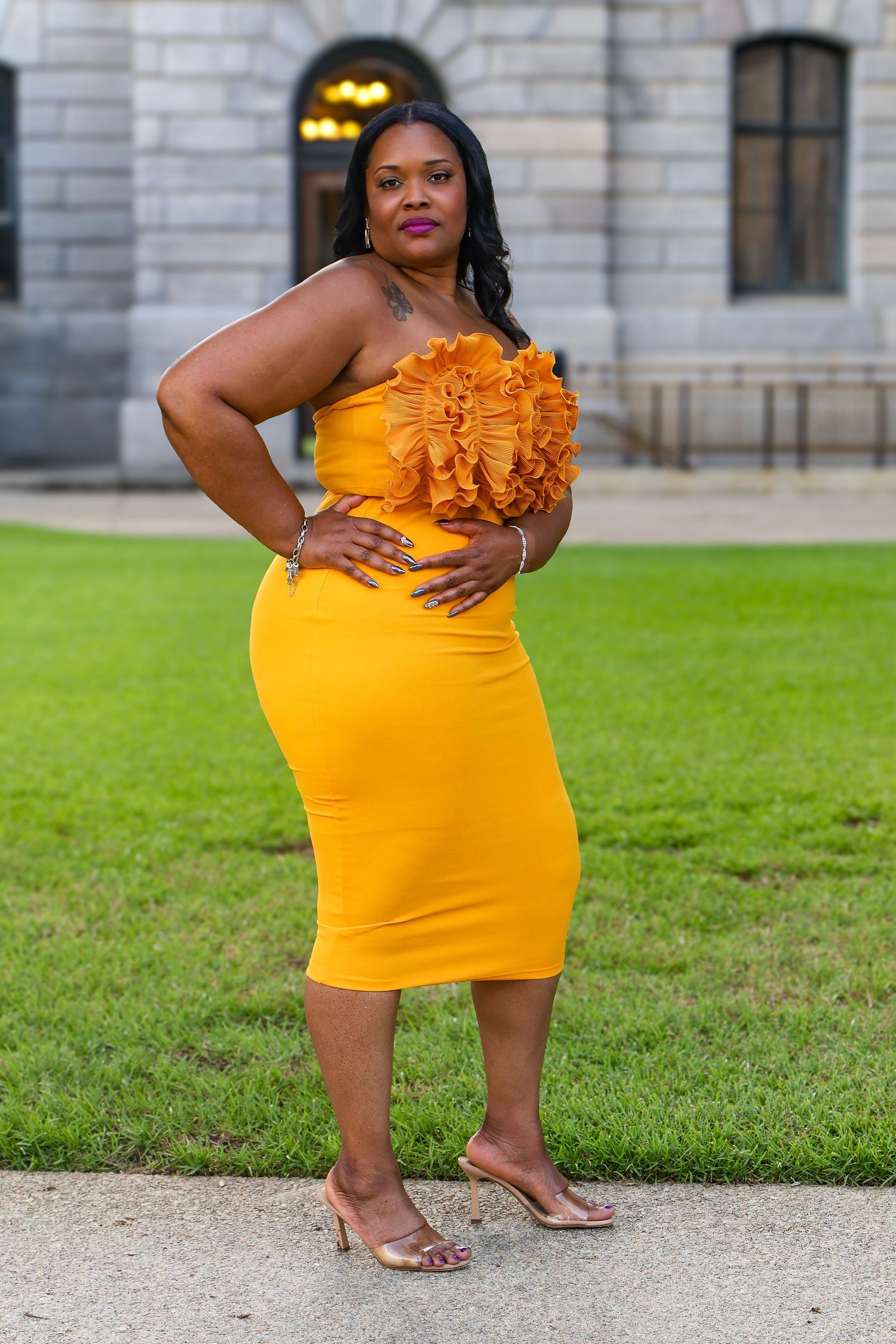 Fashion photoshoot featuring a yellow form-fitting dress with ruffle accent on a lawn.