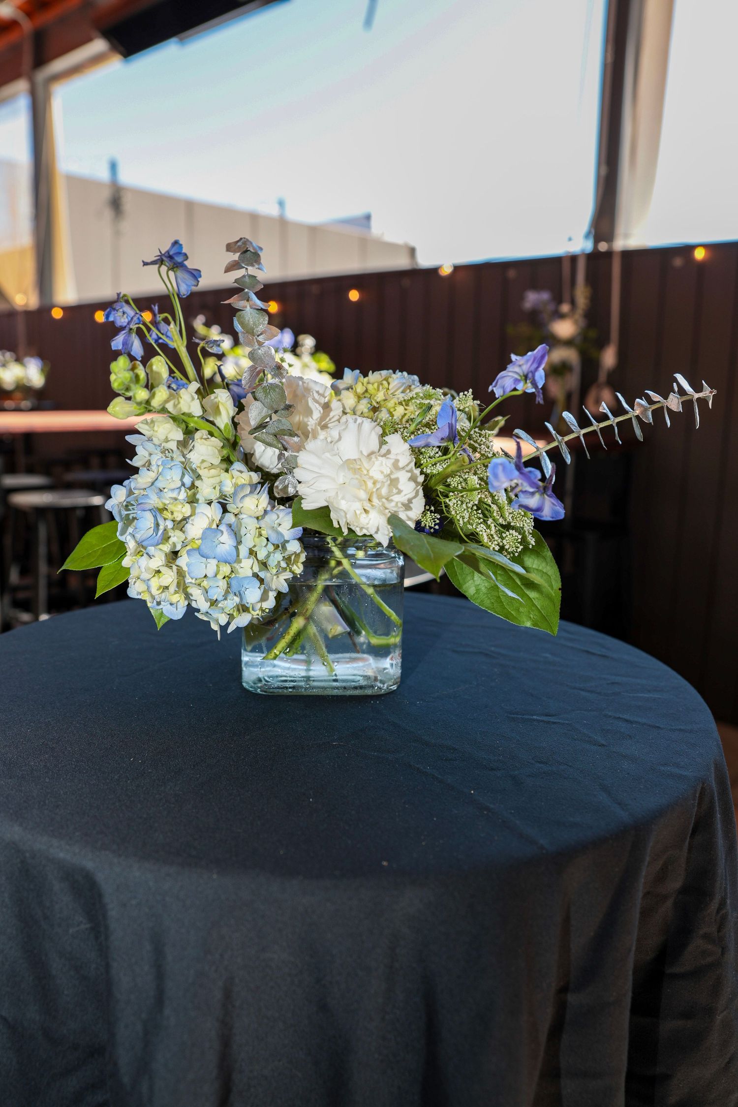 An elegant floral centerpiece with blue and white hydrangeas on a black tablecloth.