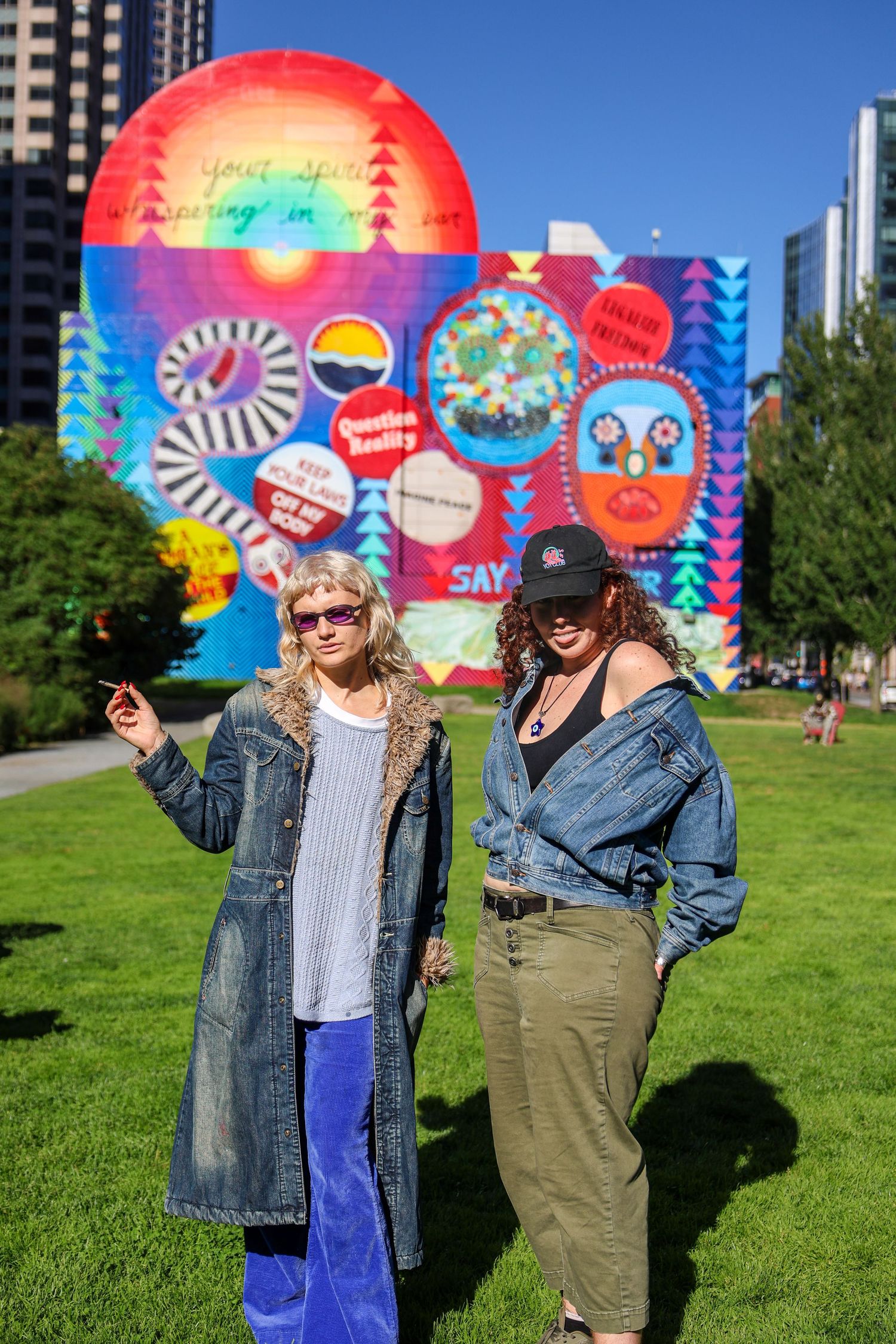 Friends strike poses against vibrant street art mural on sunny day in urban park setting.