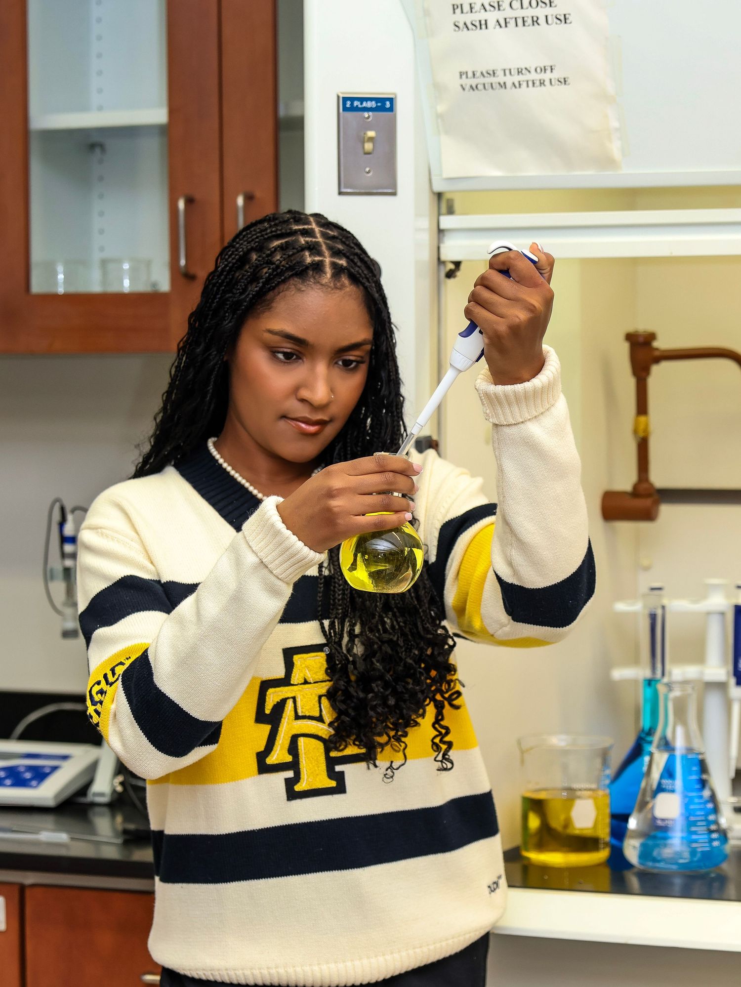 College student in varsity sweater conducts experiment in chemistry lab with colorful solutions.