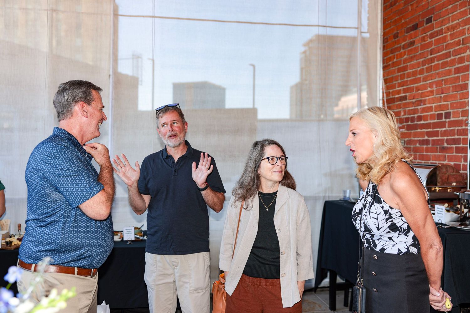 Party guests enjoying conversation in an open brick-walled event space with large windows.