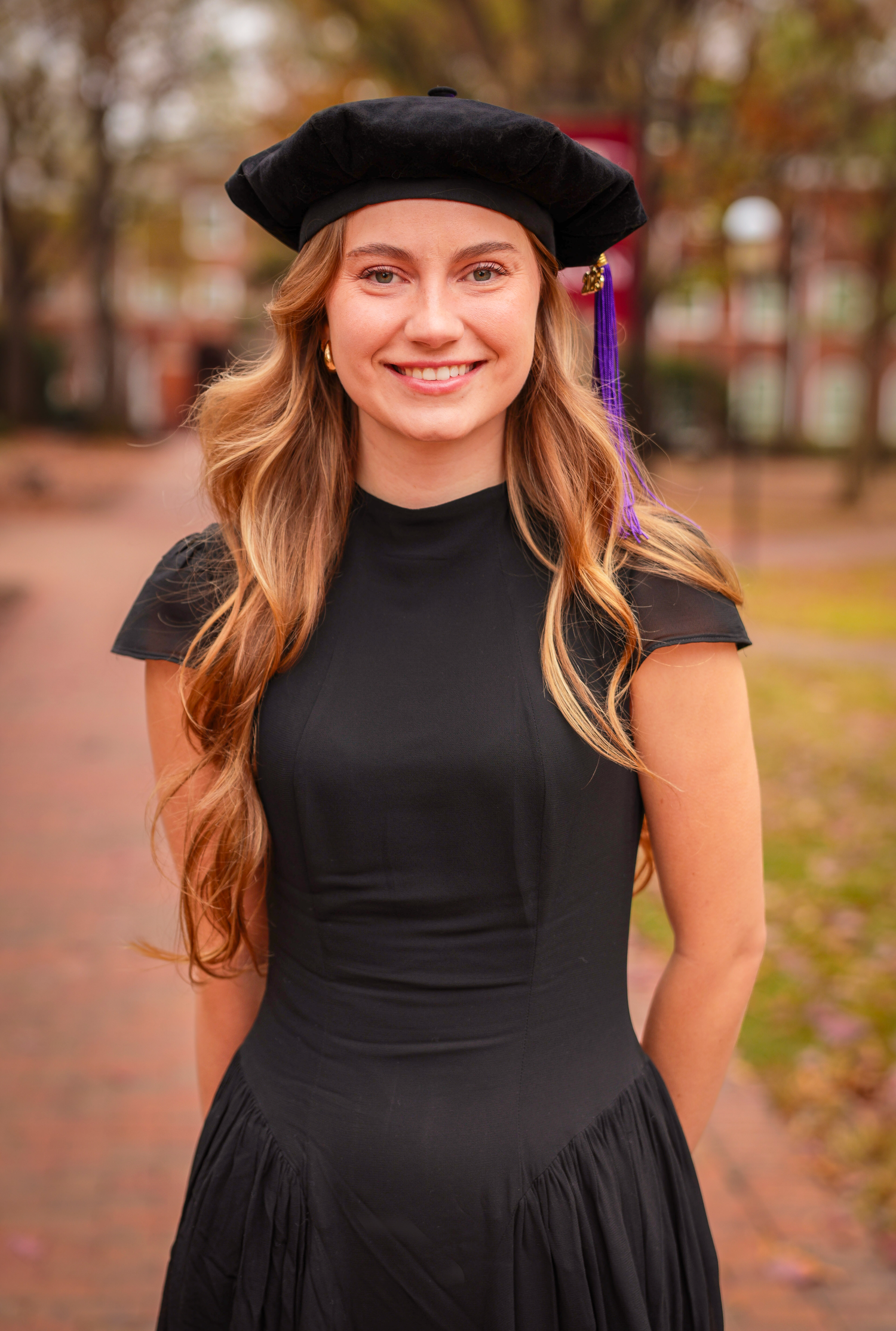 Graduate wearing a black dress and beret poses outdoors during autumn.