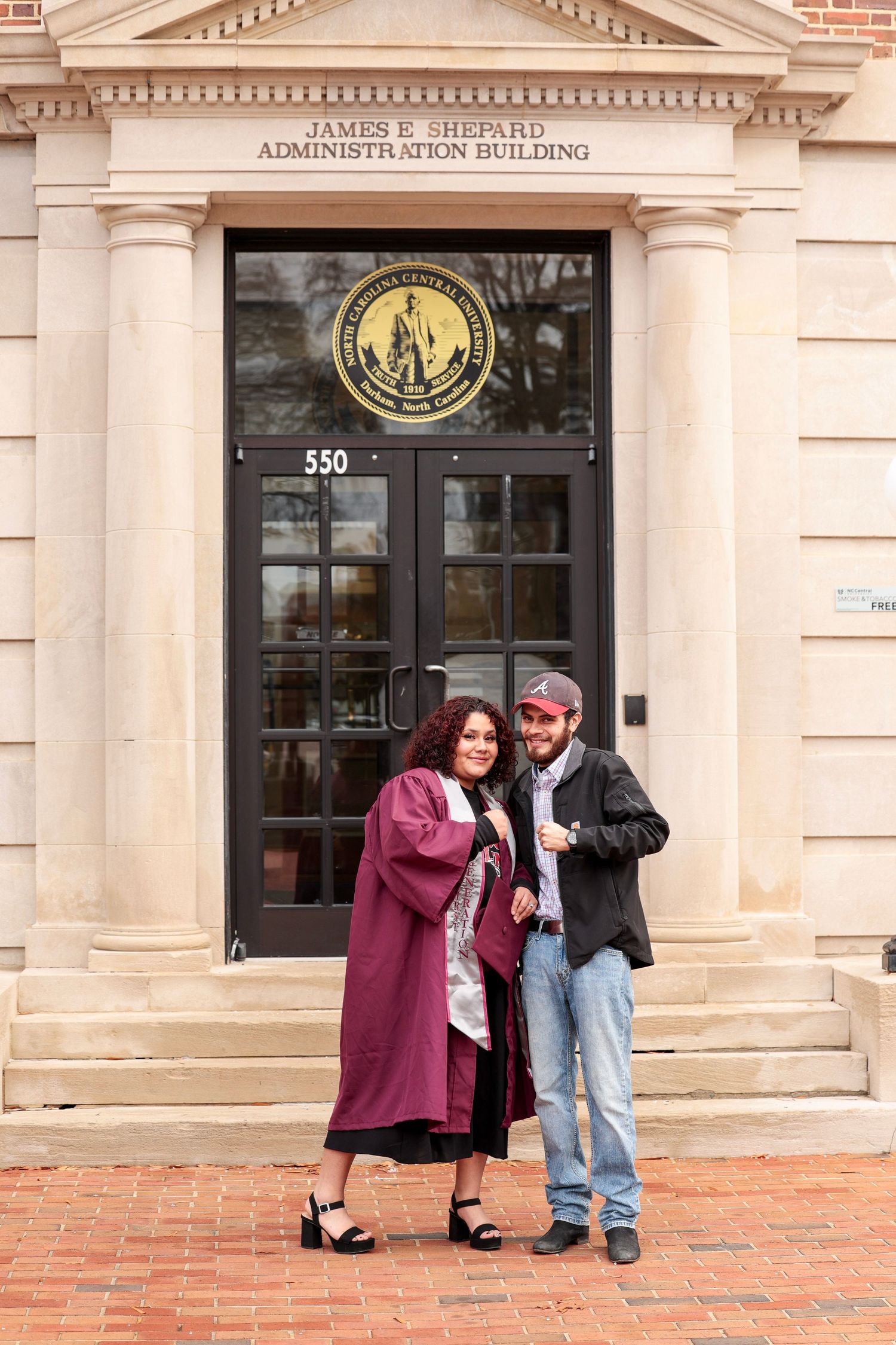 A couple poses playfully outside a brick administration building with white columns.