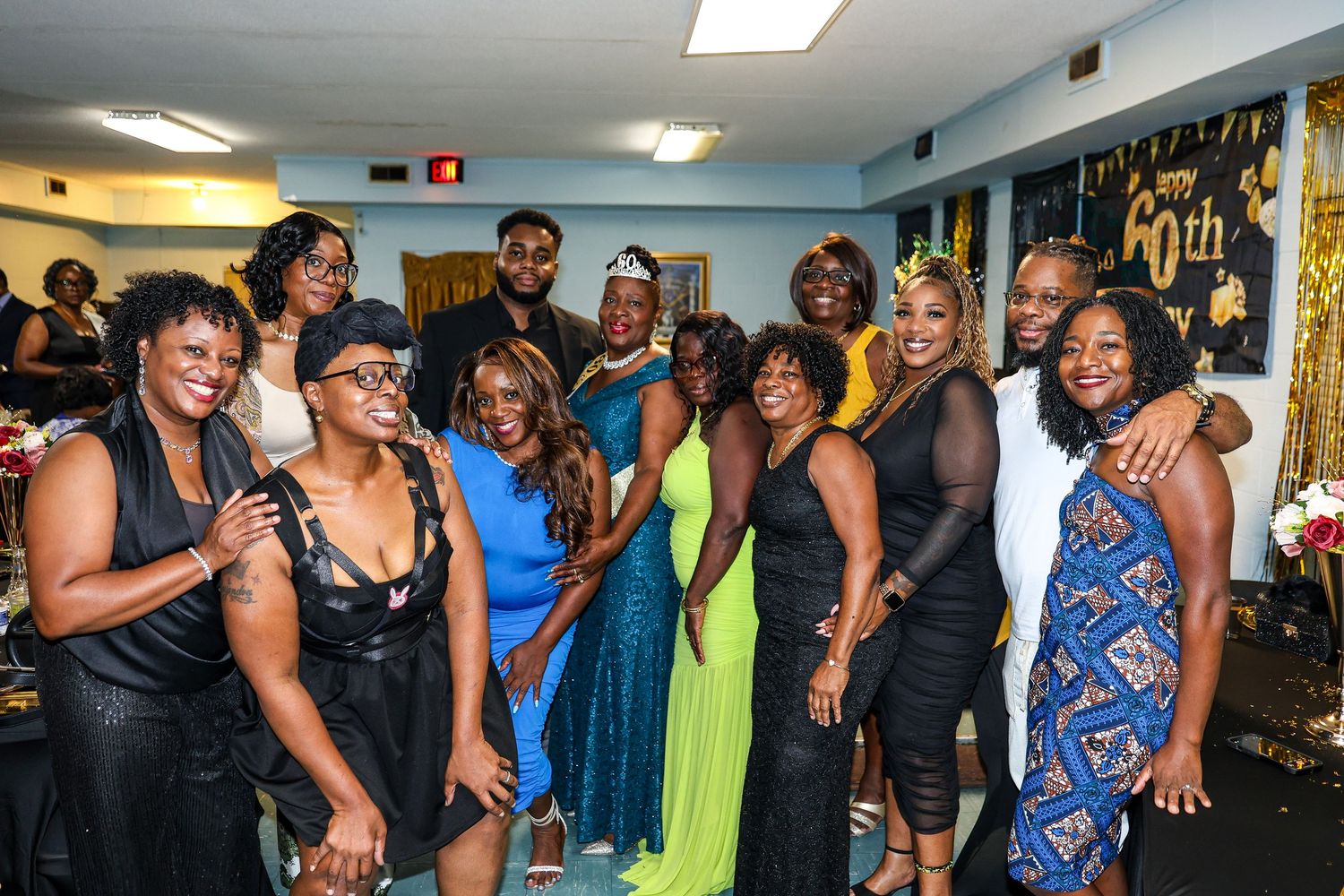 Large group of party guests in colorful formal attire gather for a celebration in an indoor venue.