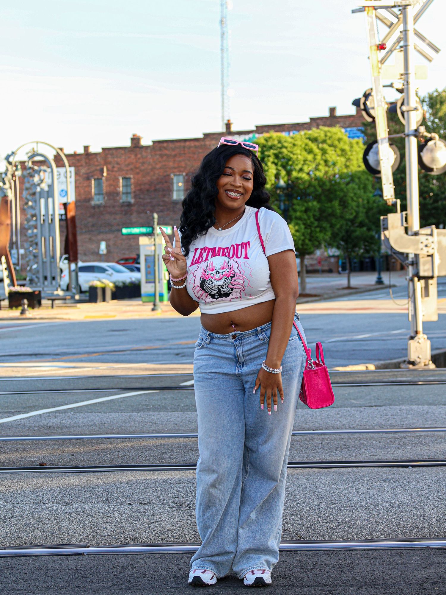 Urban street corner photoshoot with railroad crossing signals and brick buildings in background.