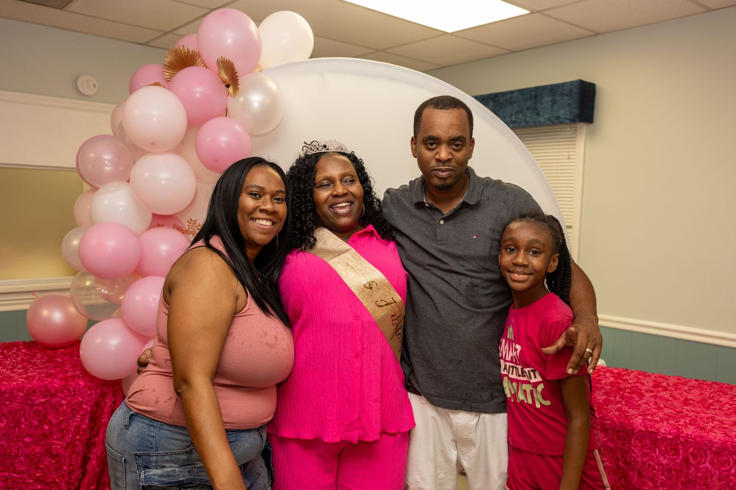 Family of four posing together at a pink balloon baby shower celebration.