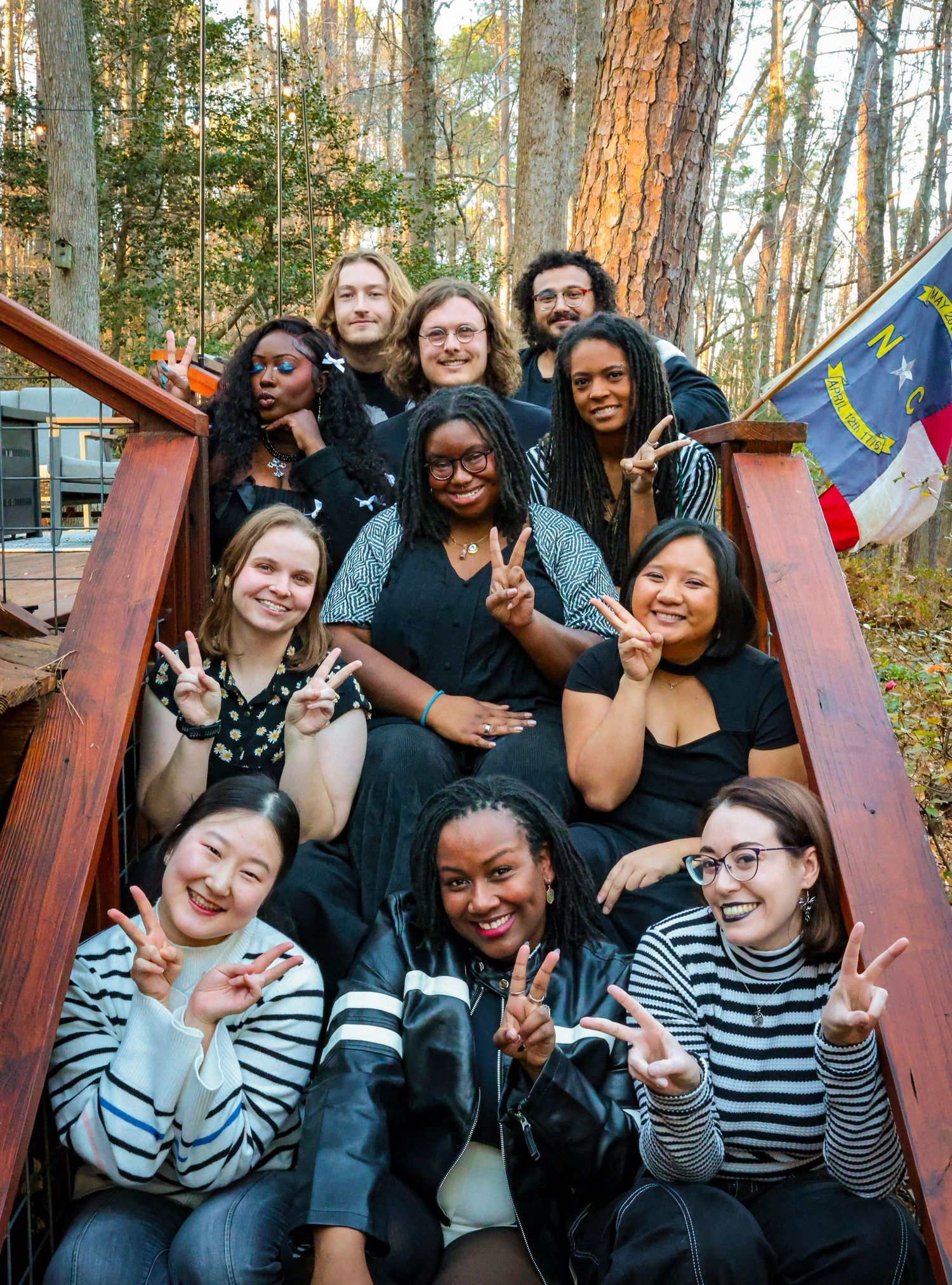 Friends posing together on wooden steps in a wooded outdoor setting.
