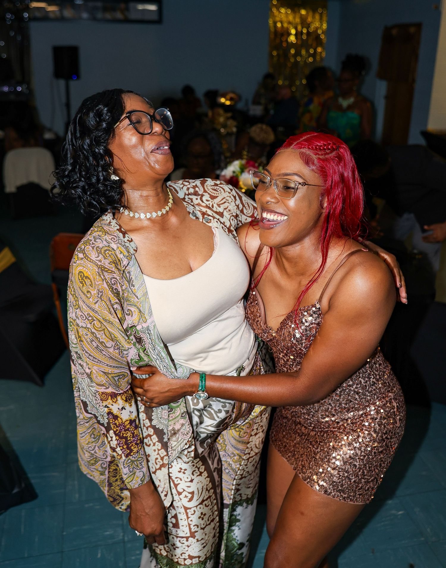 Party guests in sequined and formal attire dance and celebrate together at an indoor event.