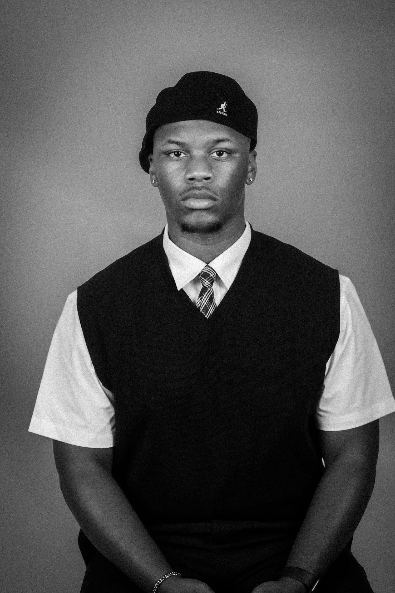 Black and white portrait of a young man wearing a black vest, striped tie, and Kangol hat.