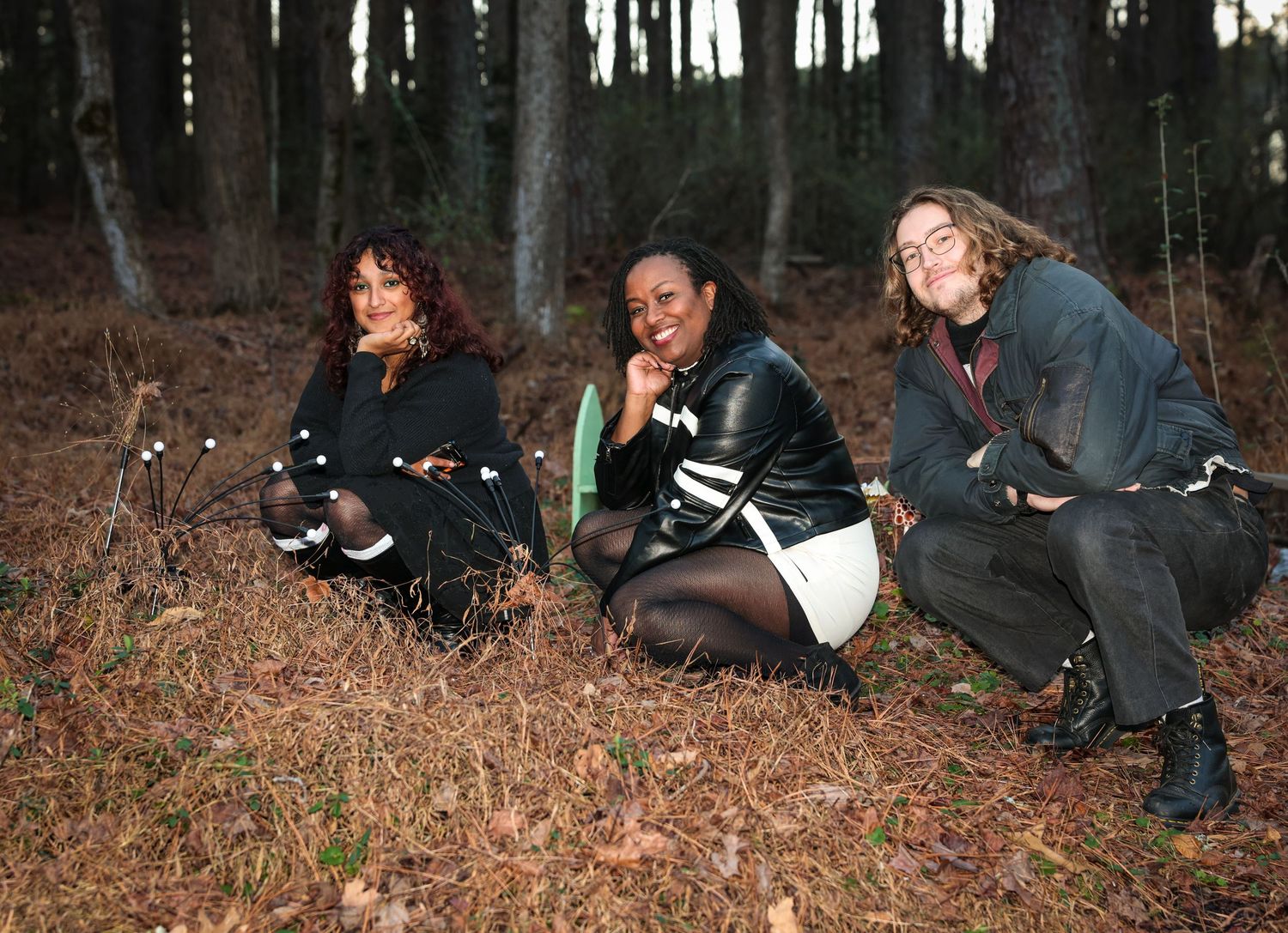 Three friends sitting casually in fallen leaves during an autumn photoshoot in the woods.