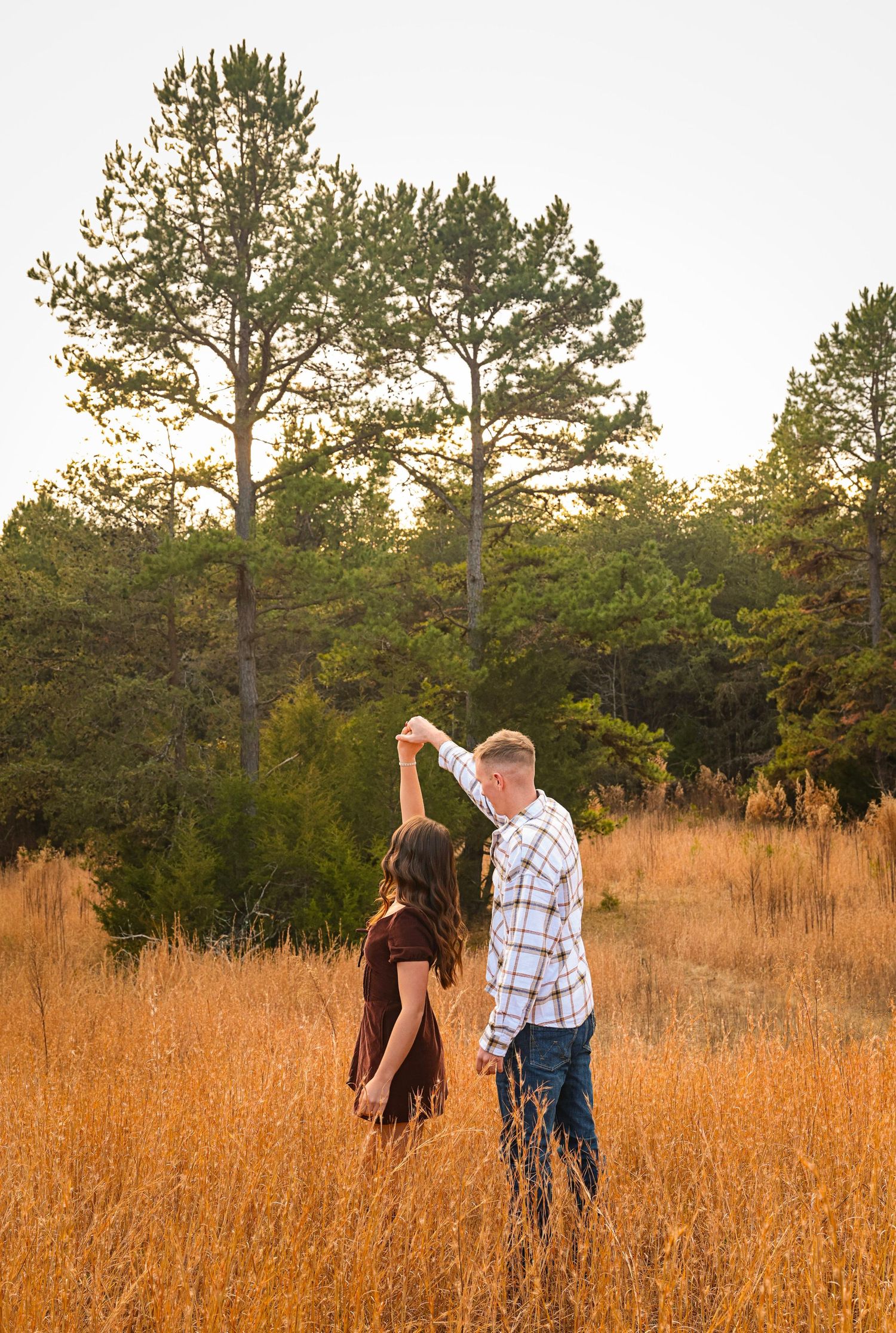 Two people stand together in a sunlit field of tall grass during golden hour.