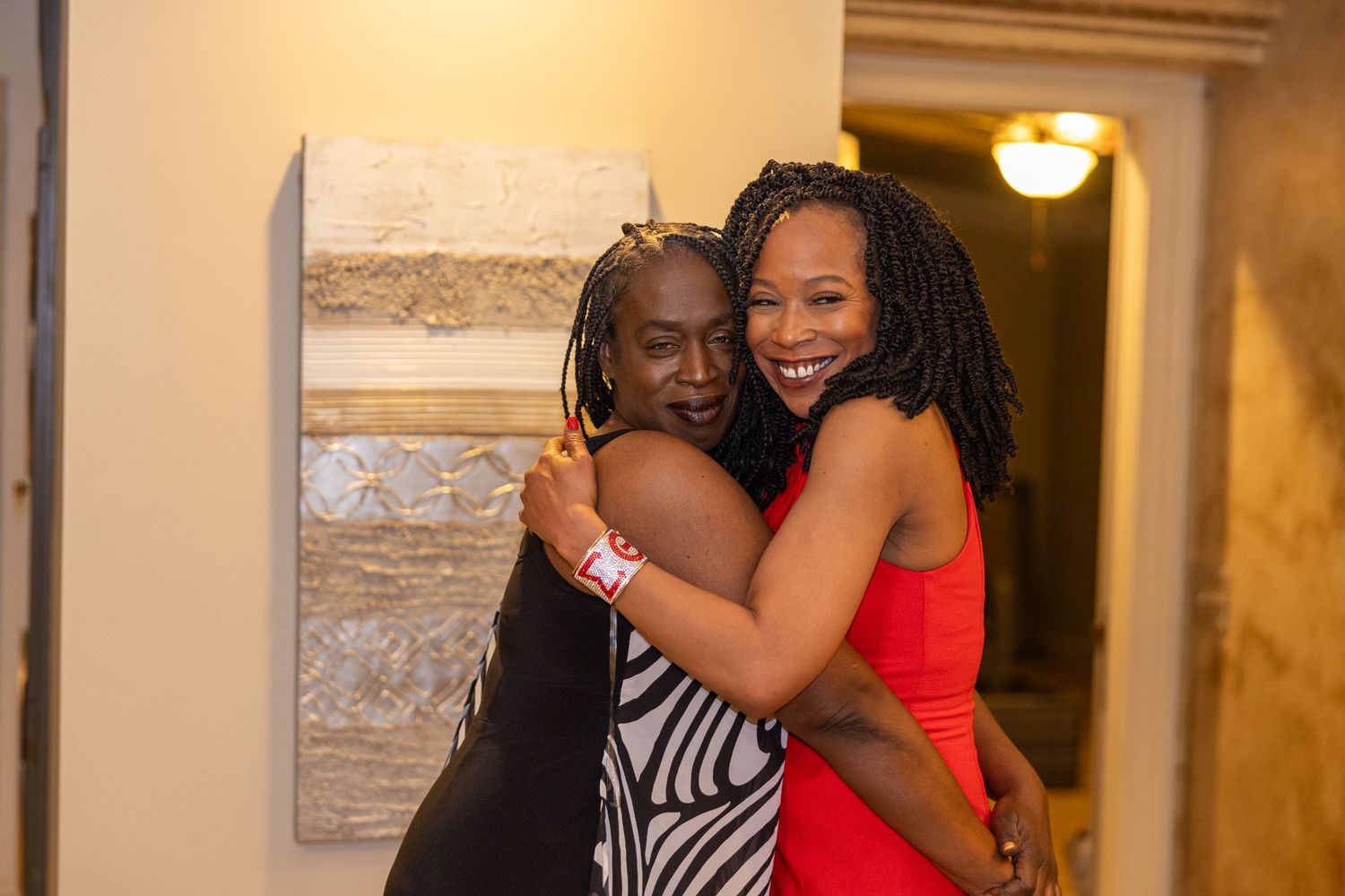 Two people share a warm embrace and joyful laughter at an indoor gathering.