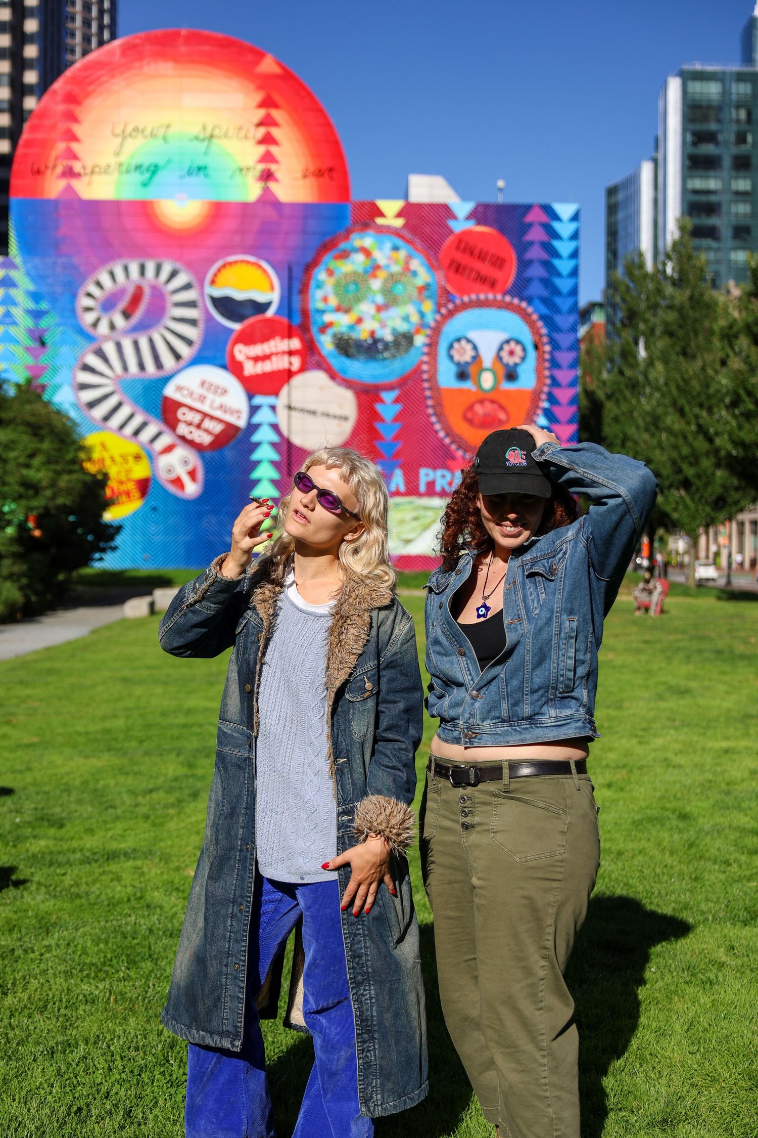 Friends enjoying sunny day with energetic poses against colorful mural in urban park setting.