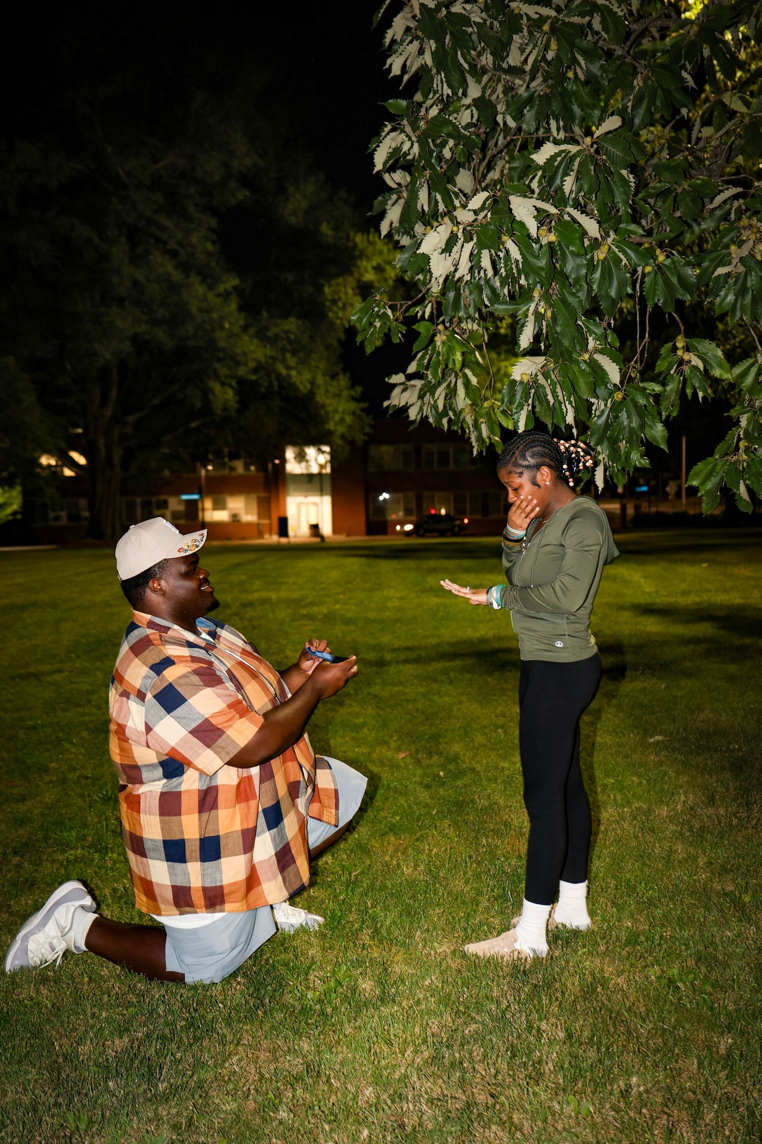A proposal moment captured on a college campus lawn at night with buildings in the background.