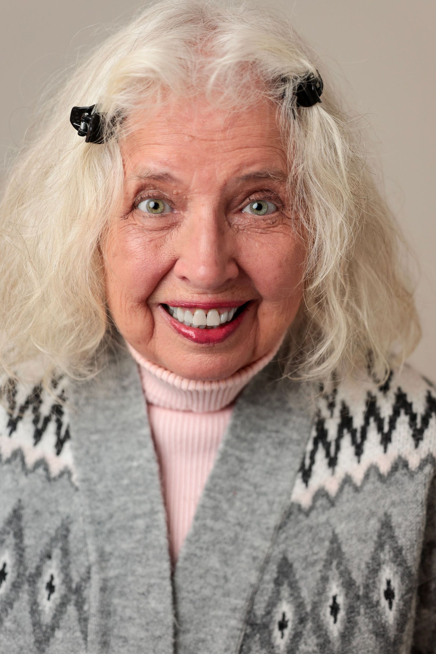 Woman with platinum hair wearing festive winter sweater and pink top against neutral background.