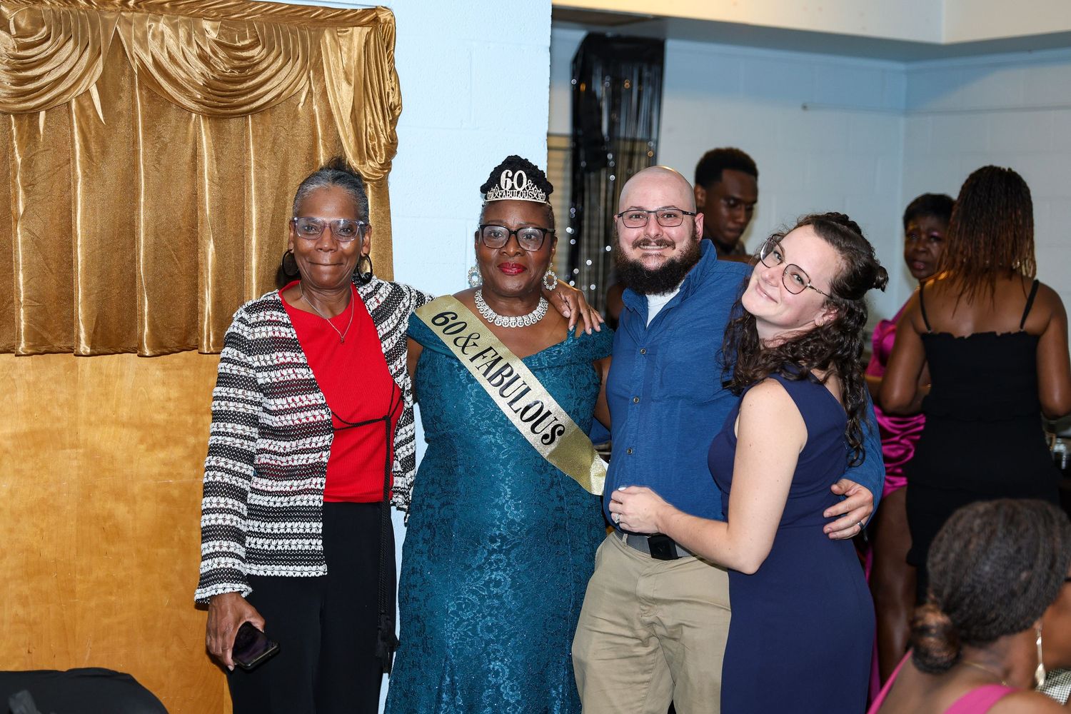 A celebratory group photo with the honoree wearing a teal dress and tiara surrounded by well-wishers.