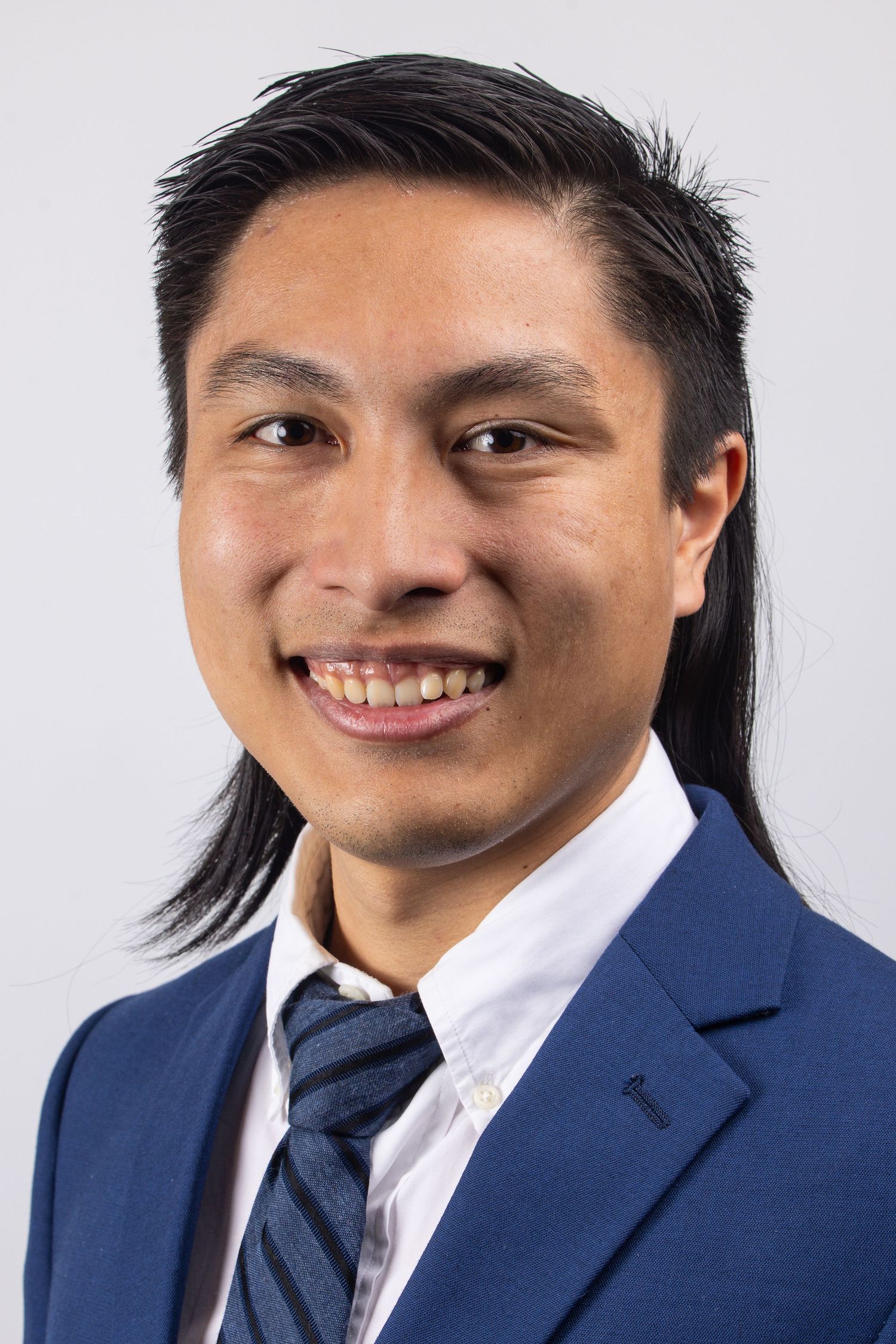 Young man in blue suit and striped tie smiling confidently in a professional headshot photo.