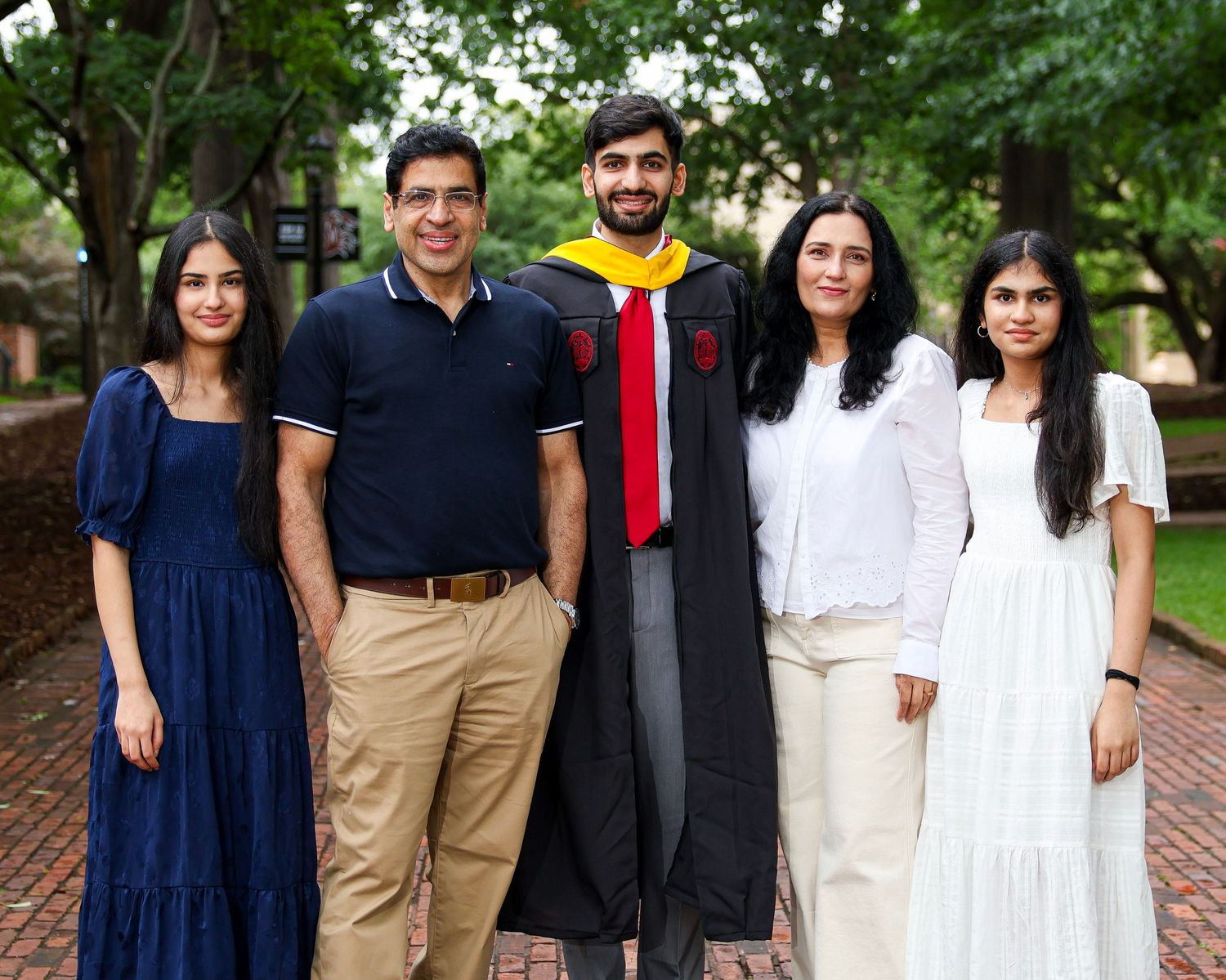 Group photo of graduates in academic regalia posing together on a brick walkway surrounded by greenery.