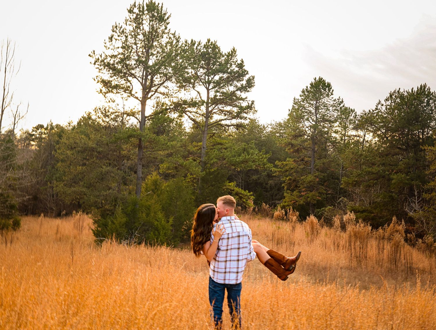 Panoramic view of couple in autumn field with pine forest at golden hour.