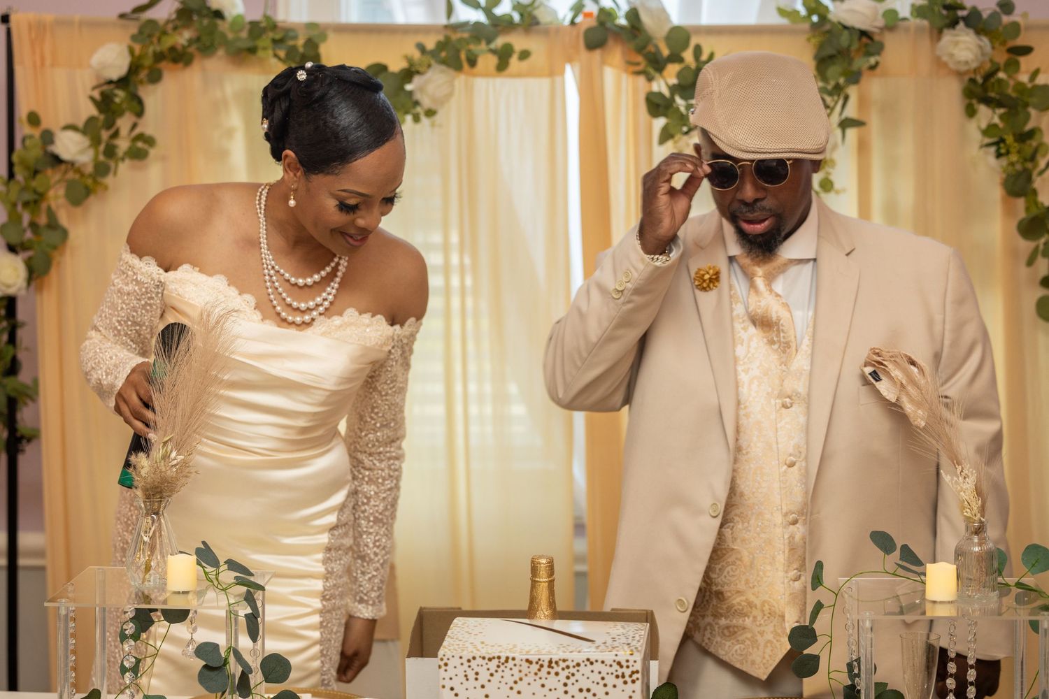 Elegant bride and groom laughing together at wedding reception under floral arch, wearing ivory and cream formal attire.