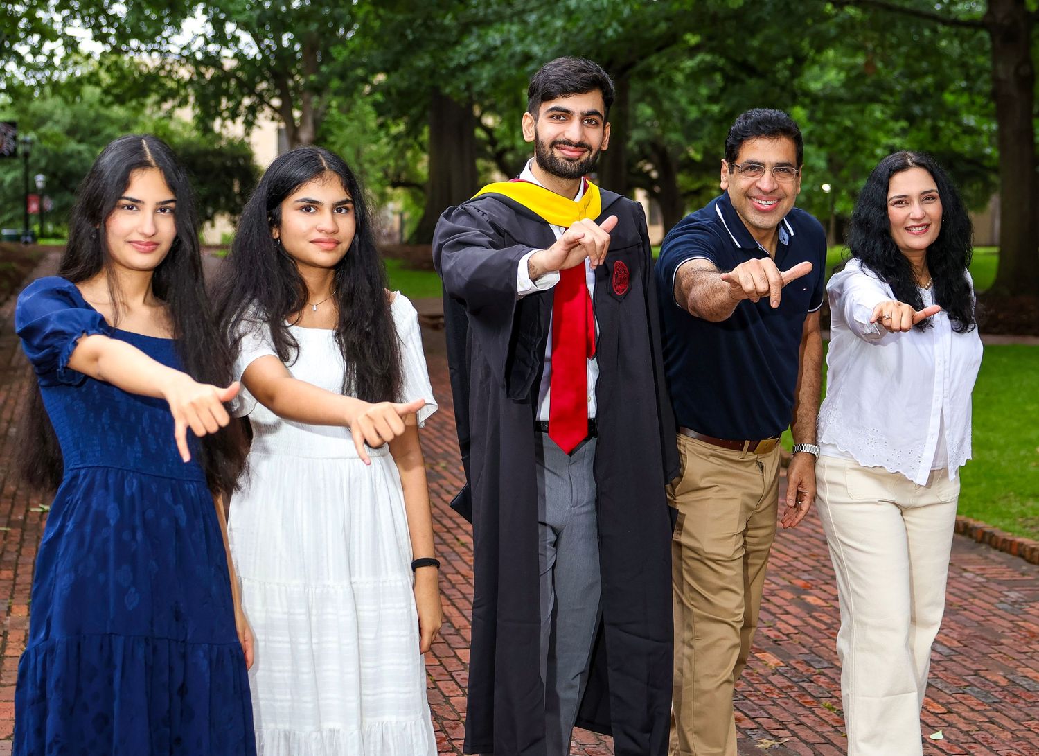 Graduates in academic regalia celebrating together outdoors on a brick pathway with green foliage.