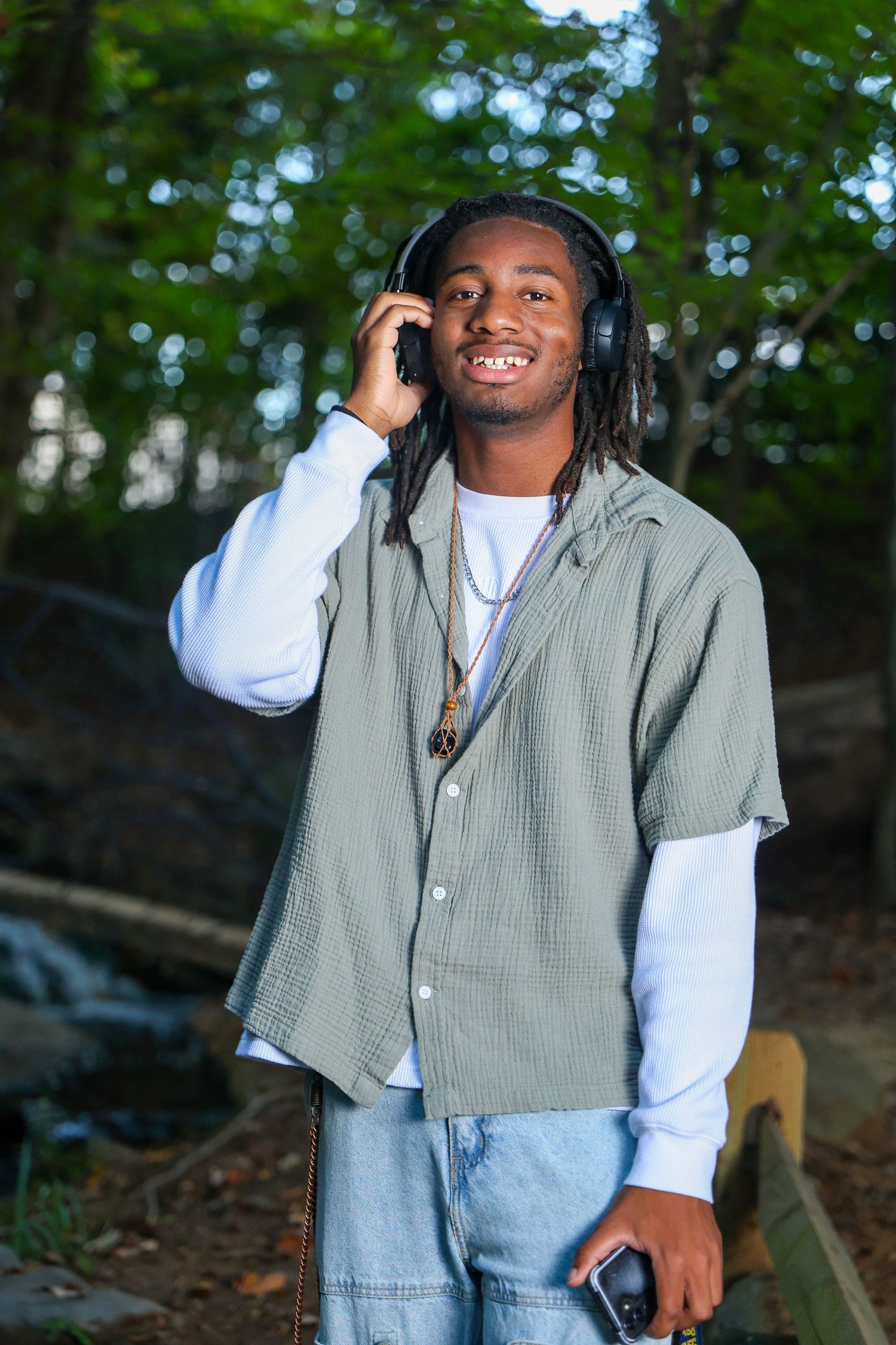 Person in casual attire with headphones enjoying a relaxed outdoor photoshoot in a wooded setting.