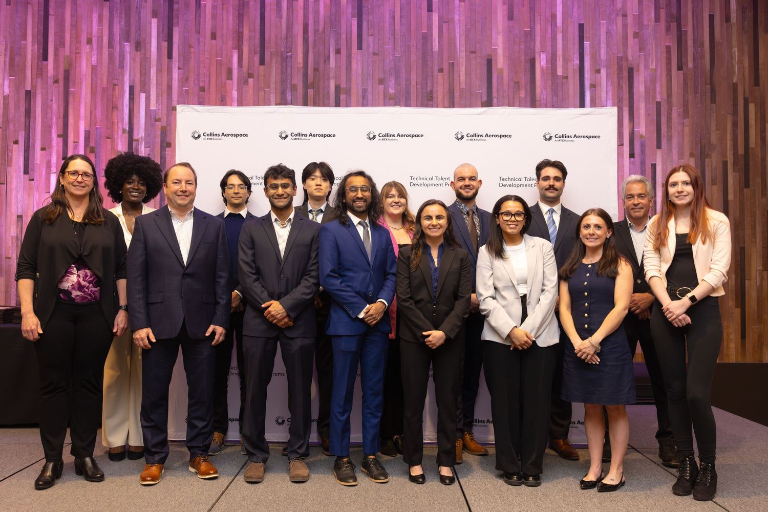 Group of professionals posing together at a corporate event in front of a decorative wooden backdrop.