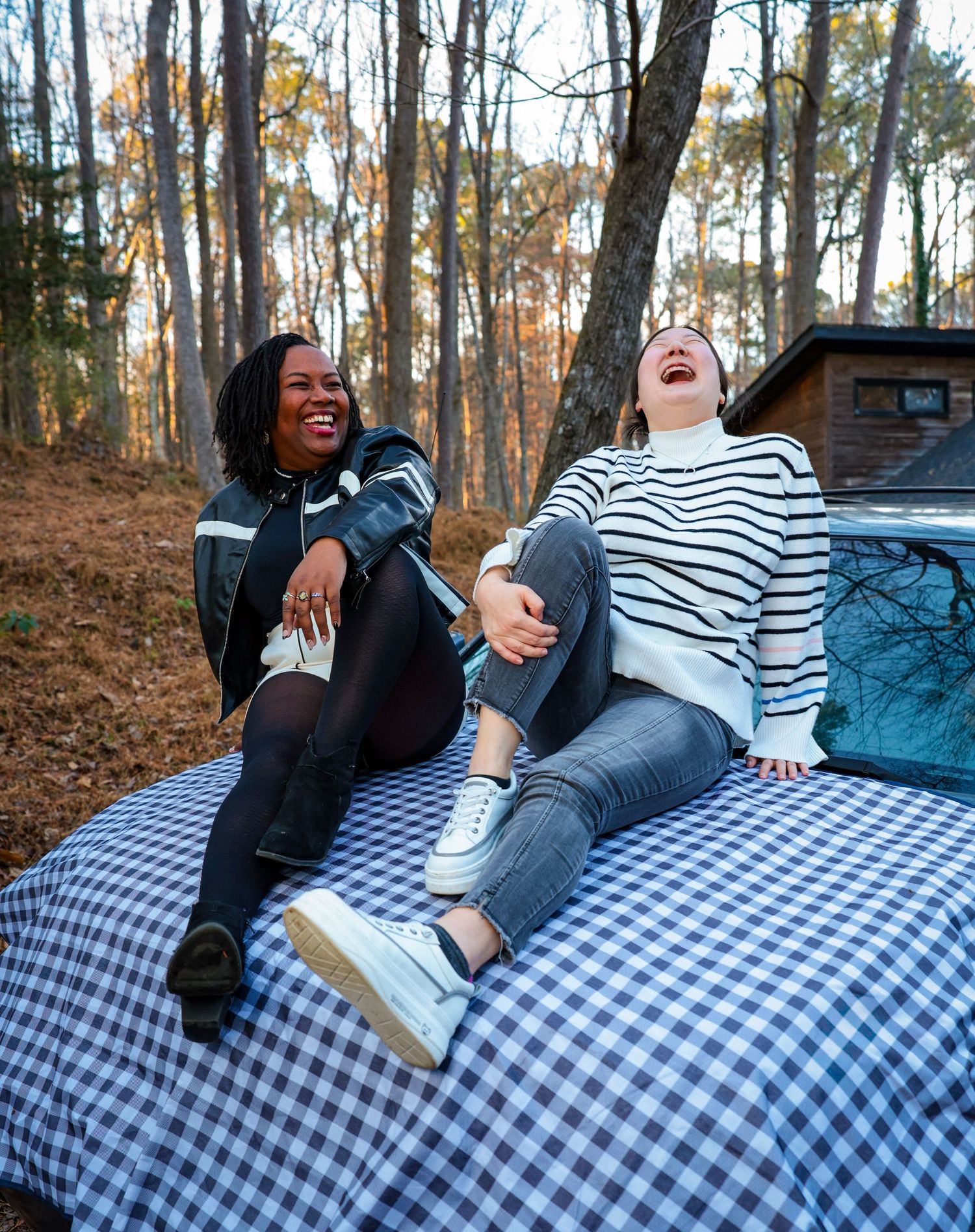 Friends relaxing on blue and white checkered blanket outdoors in wooded setting.