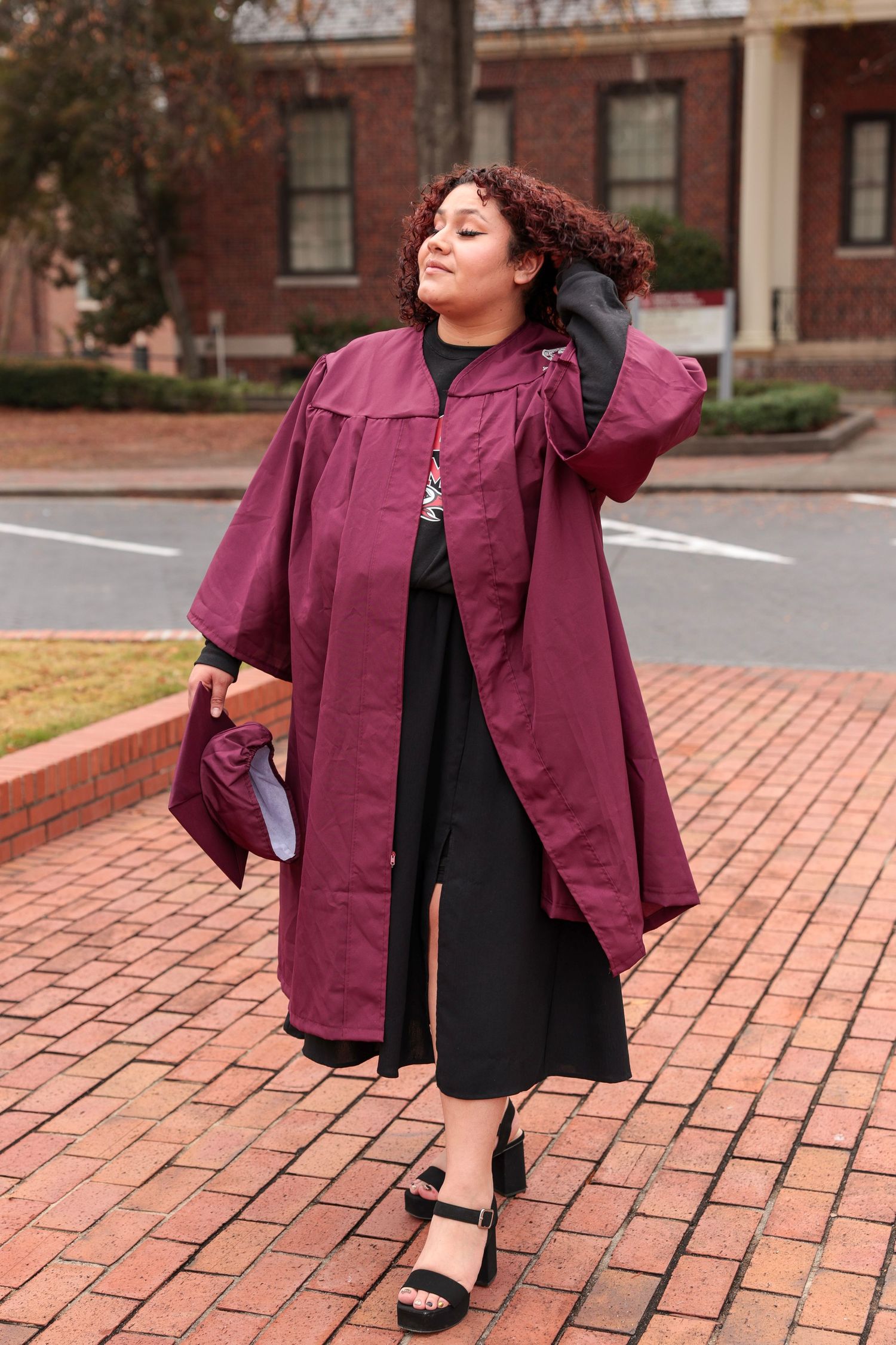 Maroon academic regalia photographed against brick courtyard background.