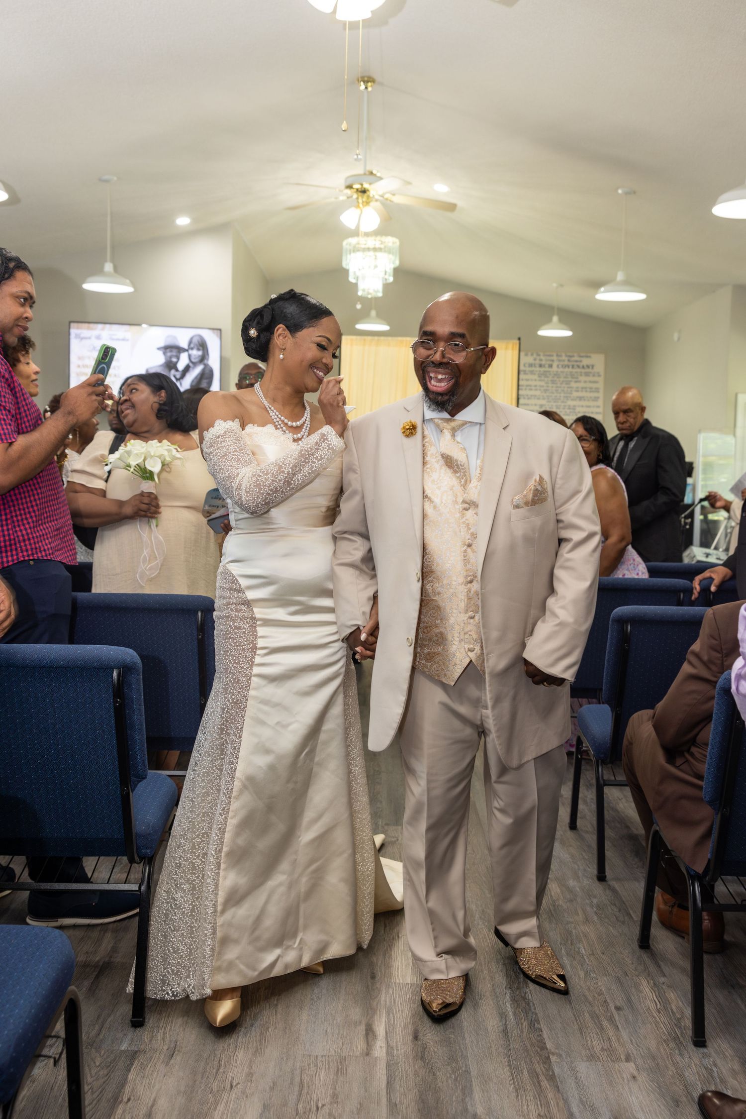 Happy newlyweds walk down the aisle in matching champagne gold wedding attire at an intimate church ceremony.